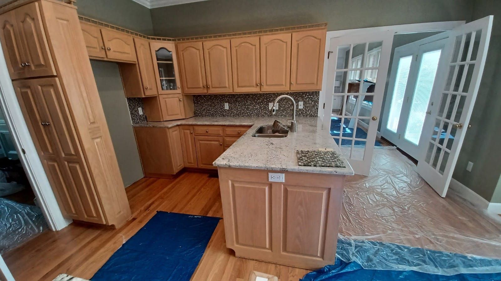 Bright kitchen with wood cabinets, granite island, blue rug, and French doors to a sunroom.