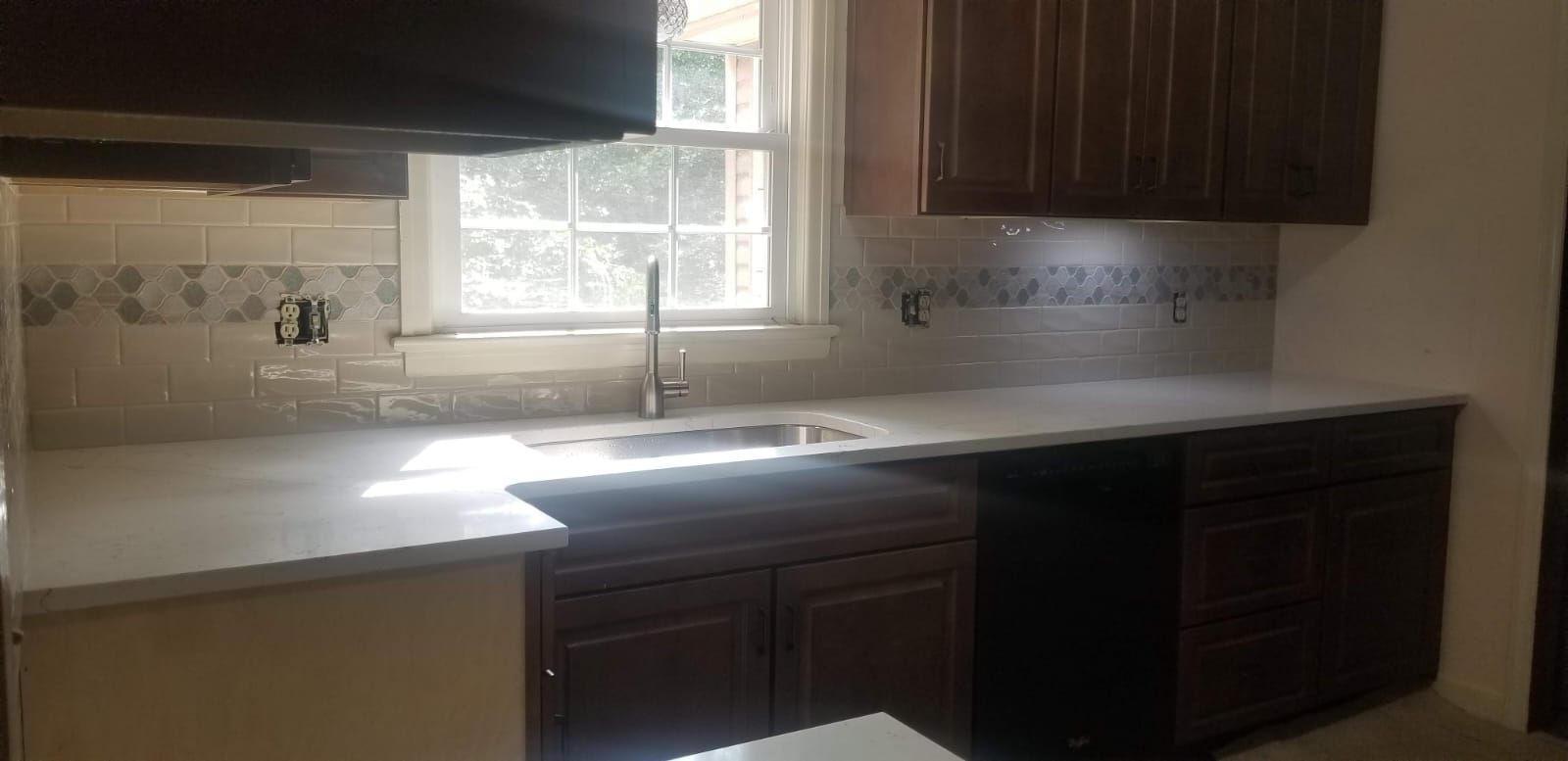 Small kitchen with white countertop, dark cabinets, double sink, and window above the sink.