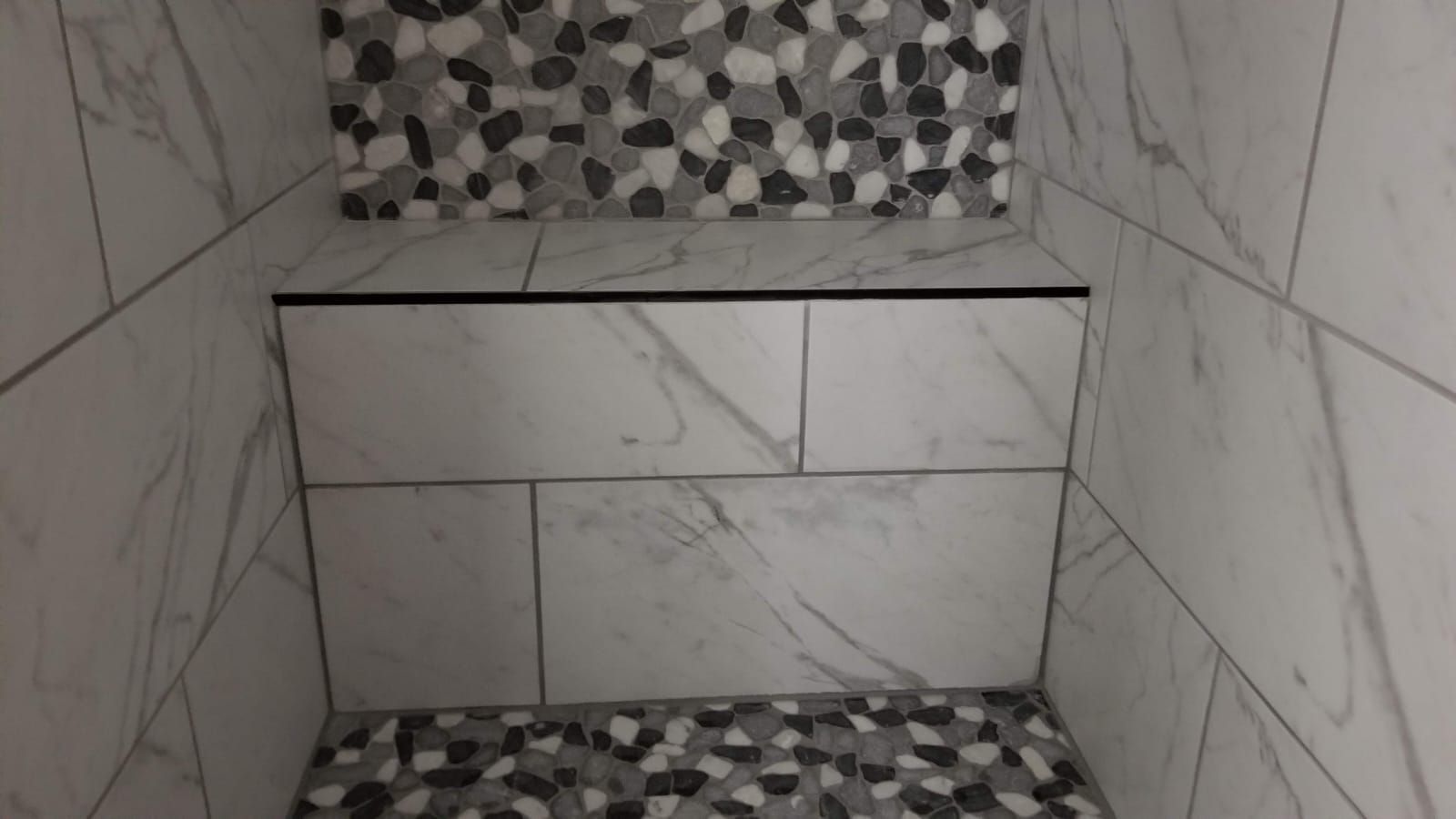 Tiled shower niche with gray marble-look walls and black-and-white mosaic trim on top and bottom