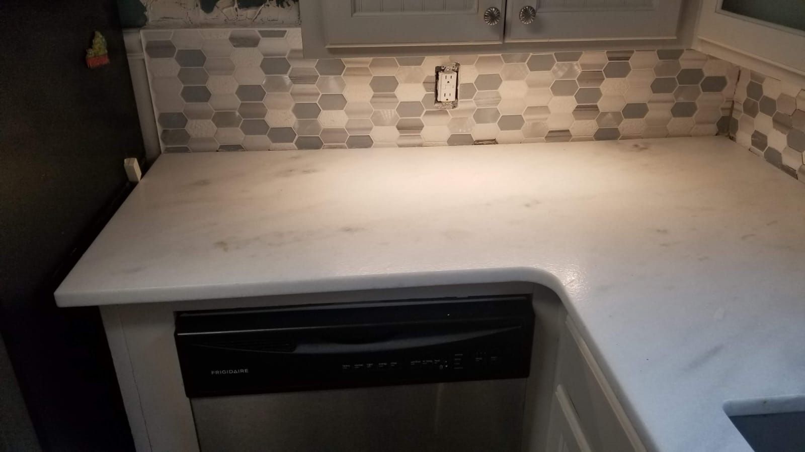 White kitchen countertop with a gray-and-white tile backsplash and a dishwasher below