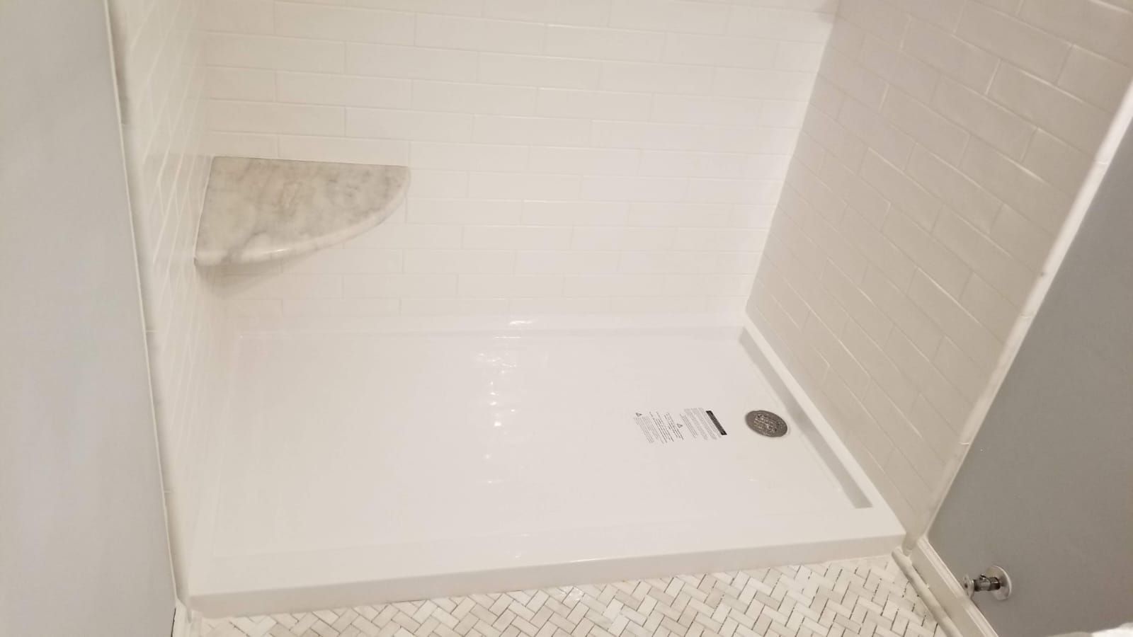 Empty white shower stall with a drain and a small wall patch on the left.