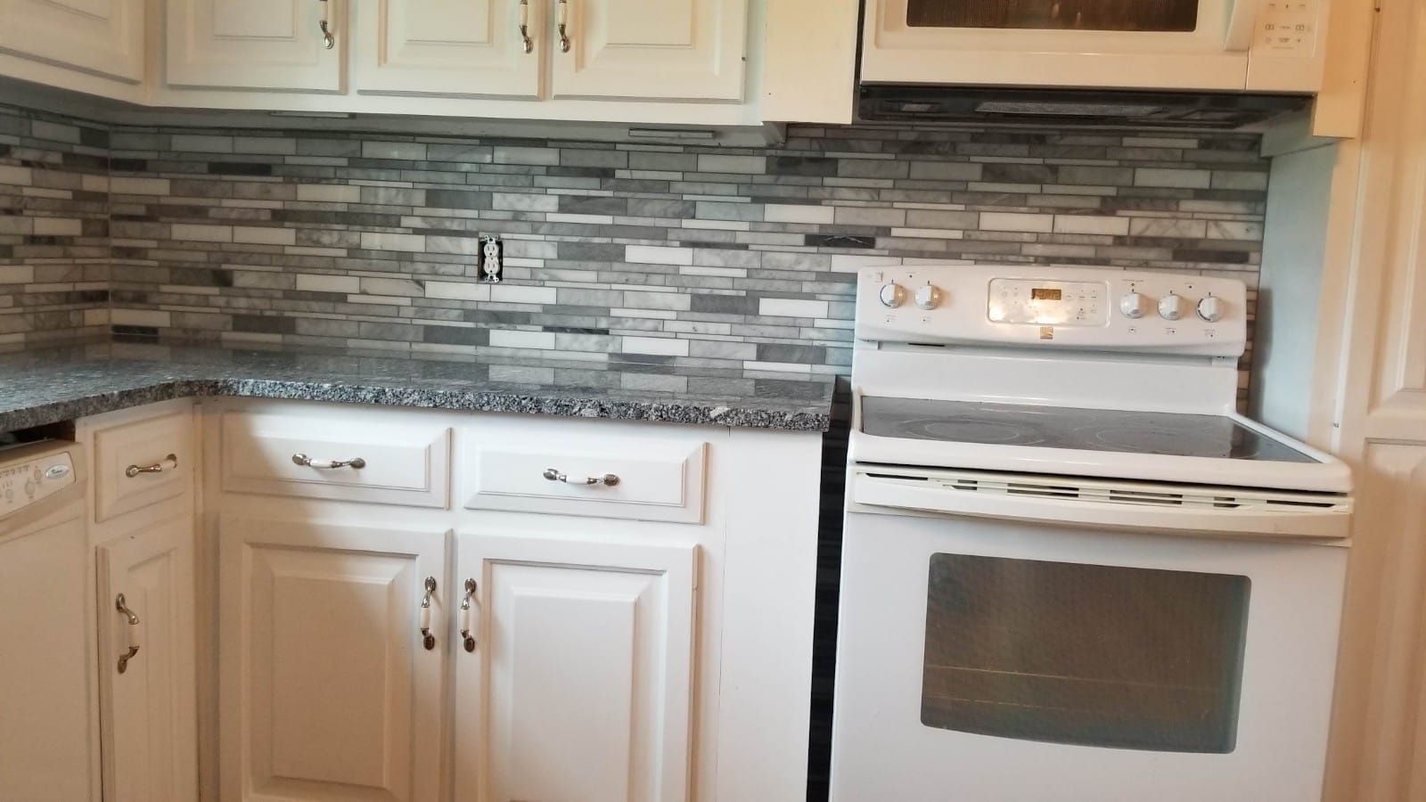 Kitchen with white cabinets, mosaic tile backsplash, and white stove and microwave.