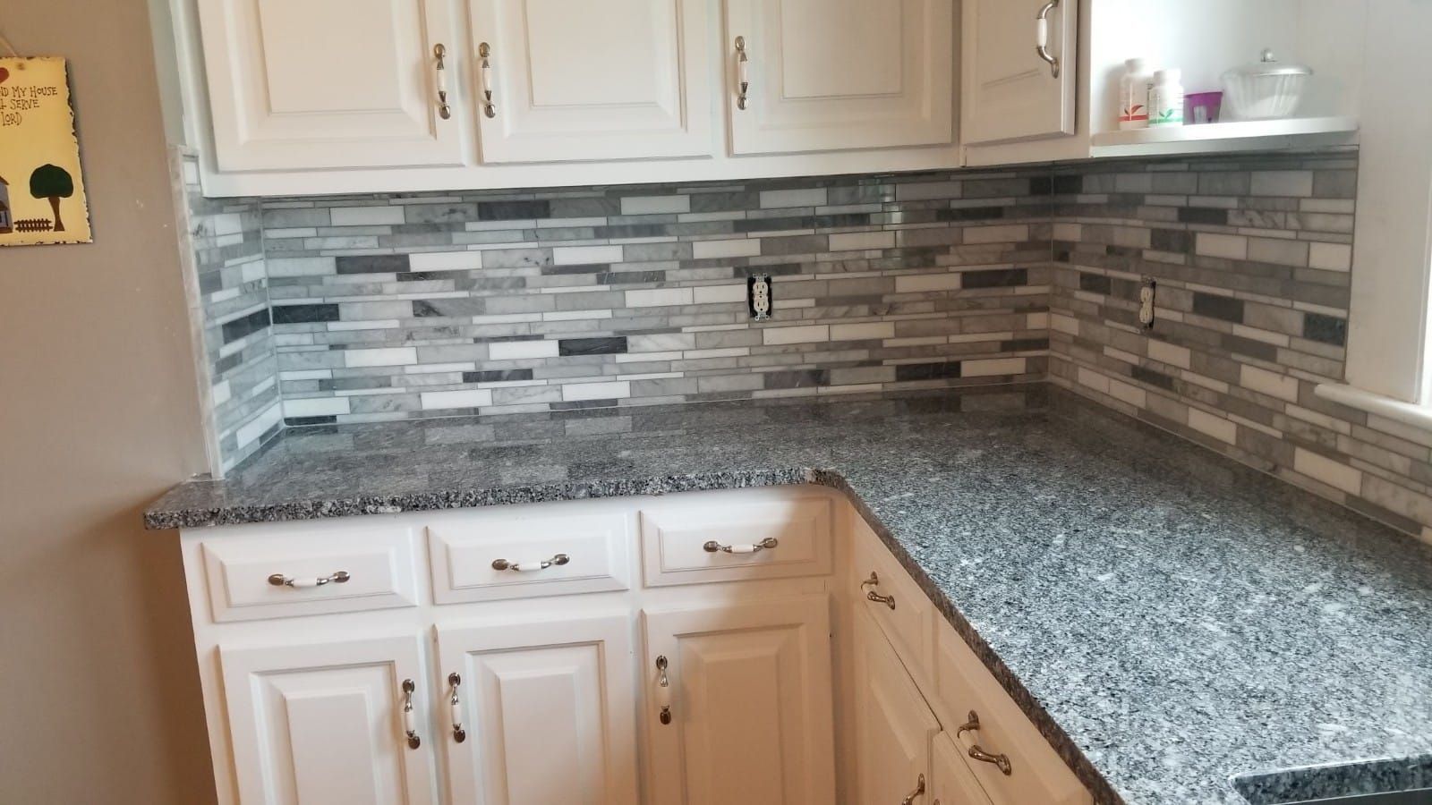 Corner kitchen with white cabinets, gray speckled countertops, and a gray mosaic tile backsplash