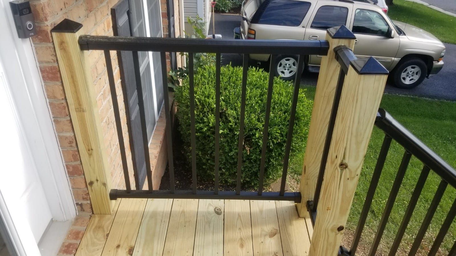 Wooden porch landing with black railing overlooking a driveway and parked cars