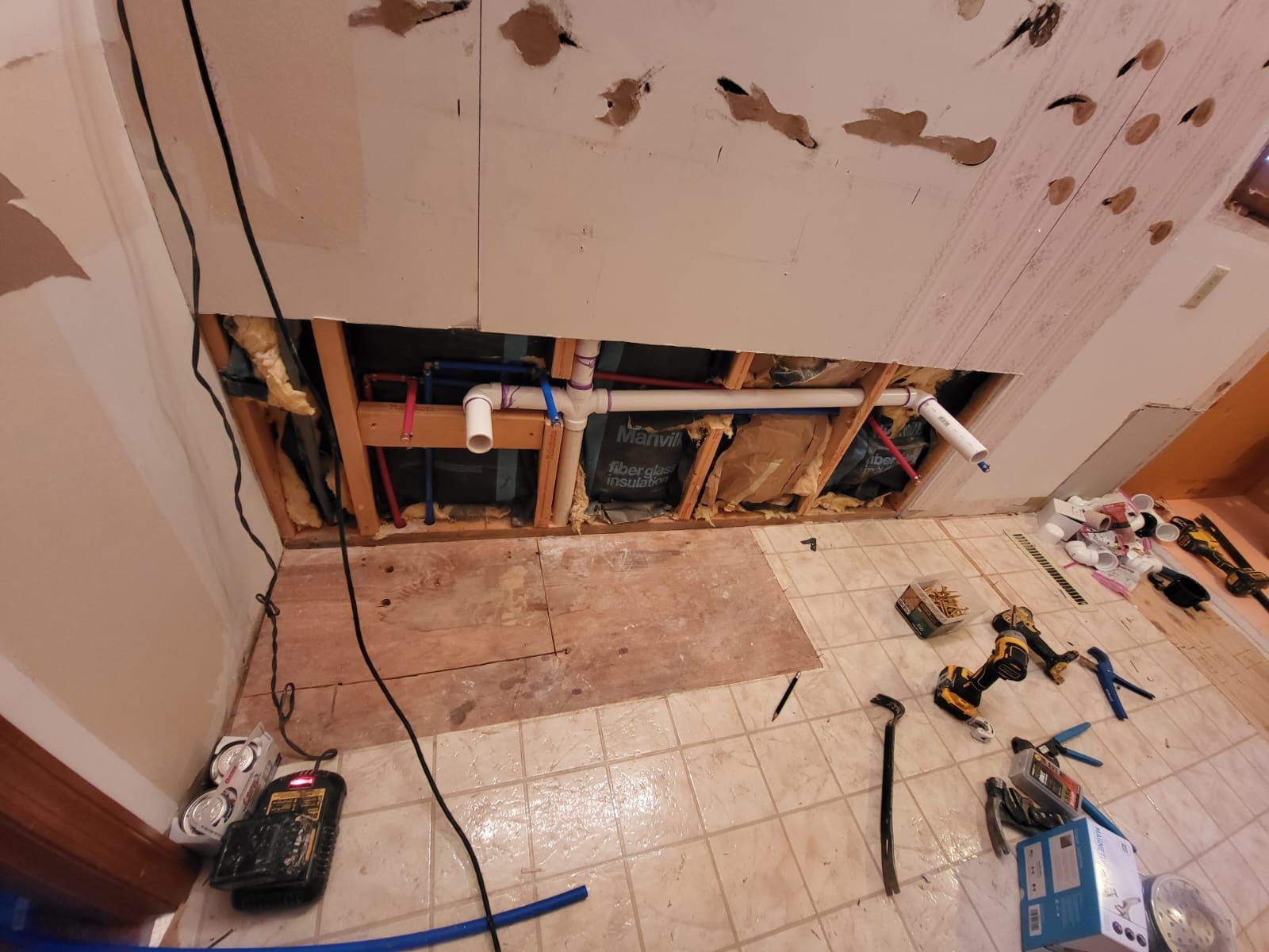 Bathroom under renovation with exposed wall framing, tools, and tile debris on the floor.