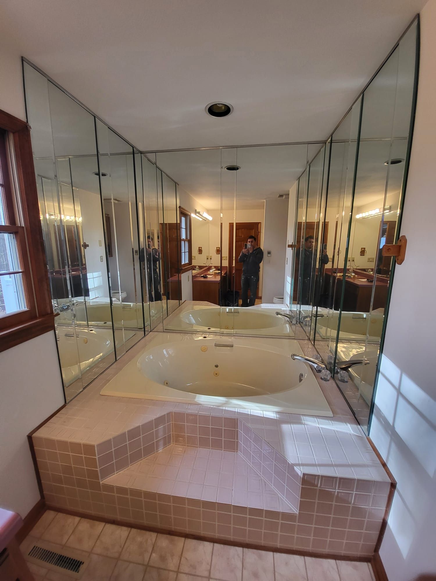 Indoor bathroom with a white tiled jacuzzi tub and mirrored walls in a narrow hallway-like room