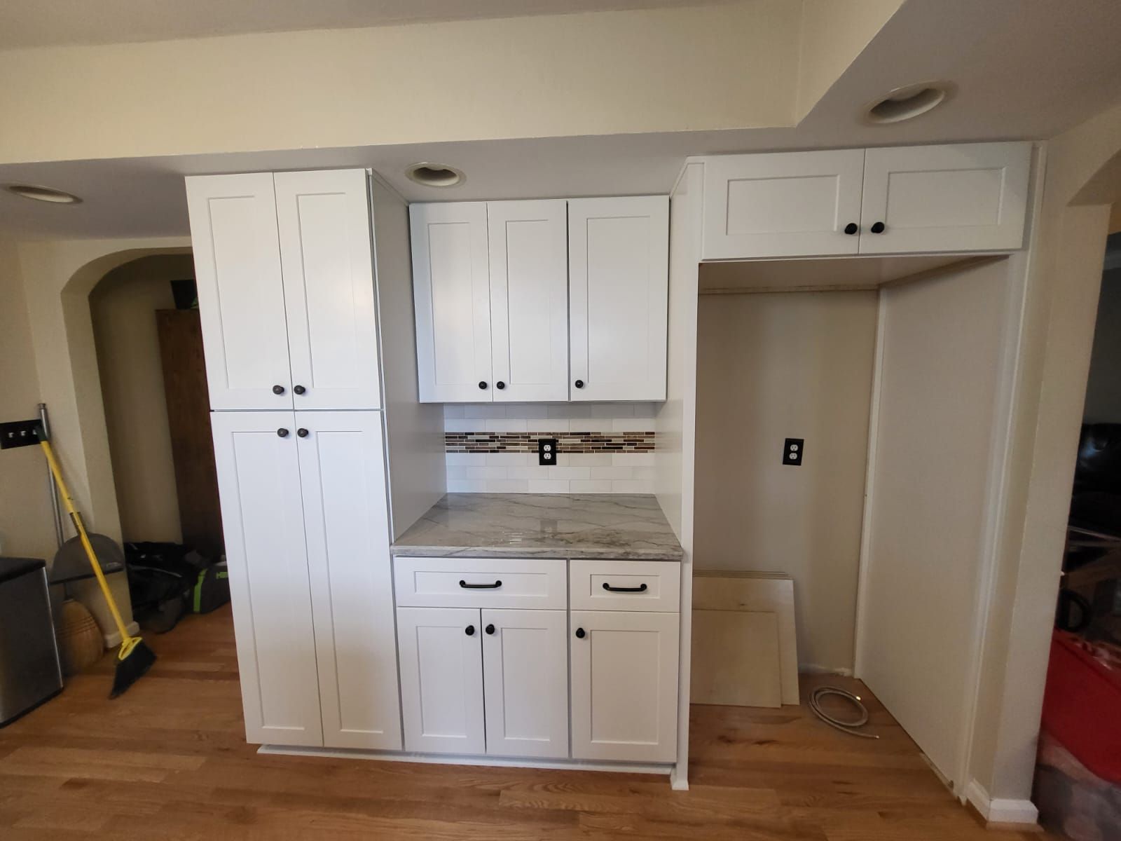White kitchen cabinets installed in an unfinished room with exposed walls and hardwood floor