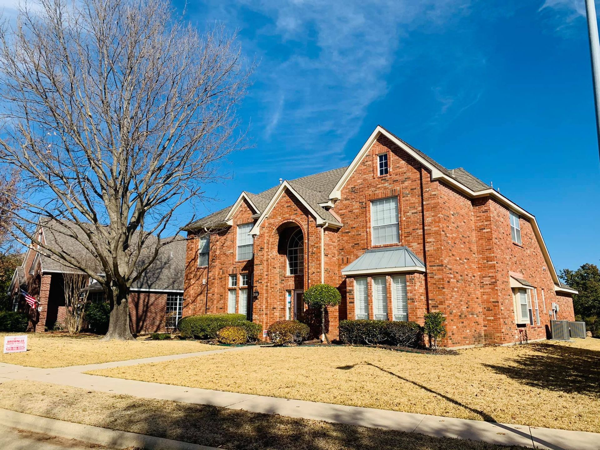 A large brick house with a tree in front of it on a sunny day.