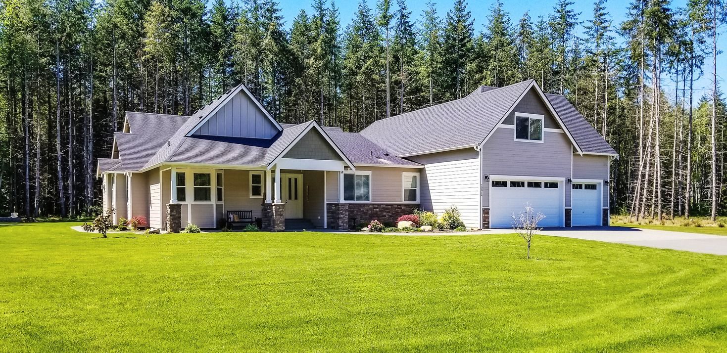 A large house is sitting on top of a lush green field surrounded by trees.