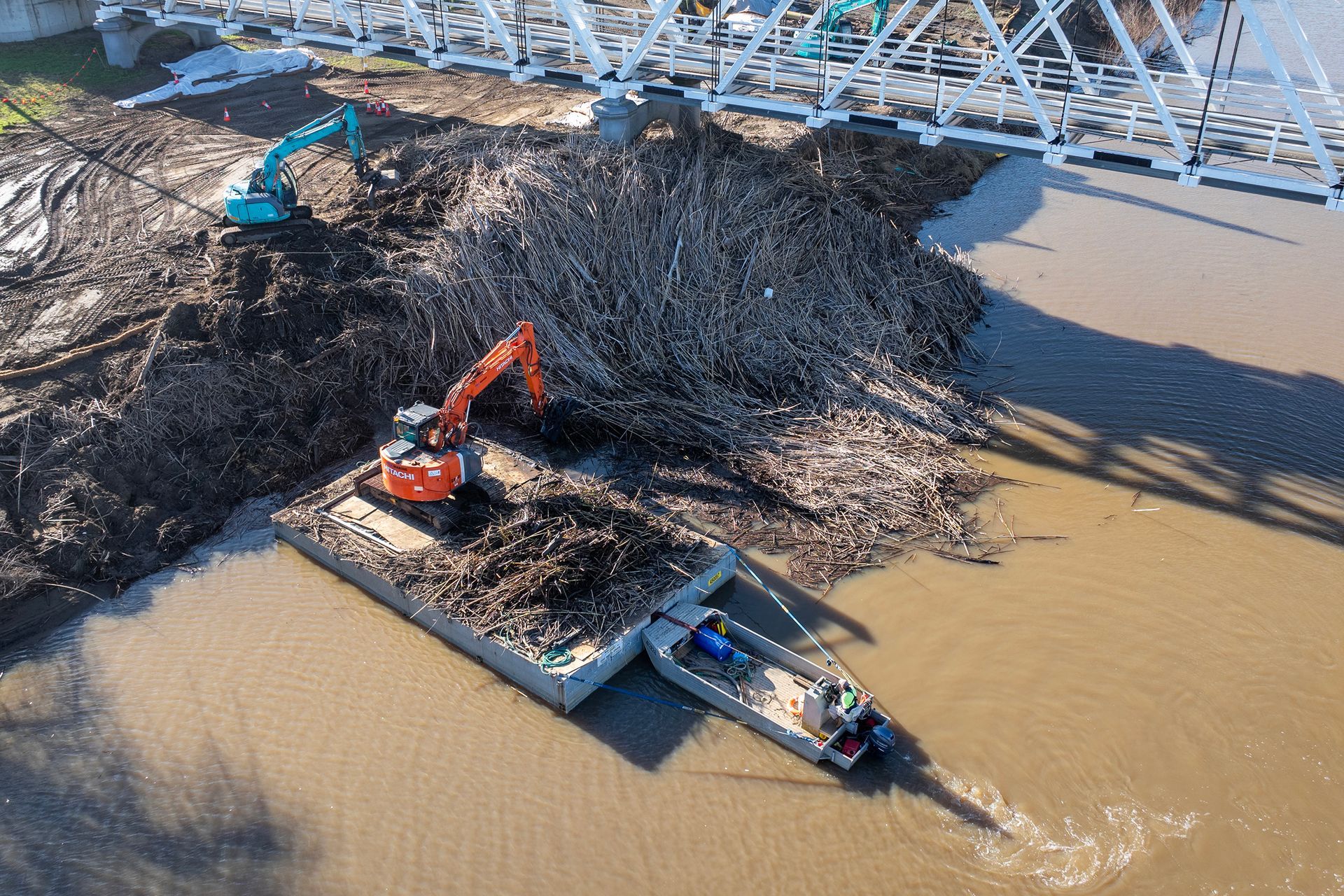 An Excavator and A Blue Excavator on Shore Clear Large Amounts of Driftwood — M&J Marine Services in Medowie, NSW