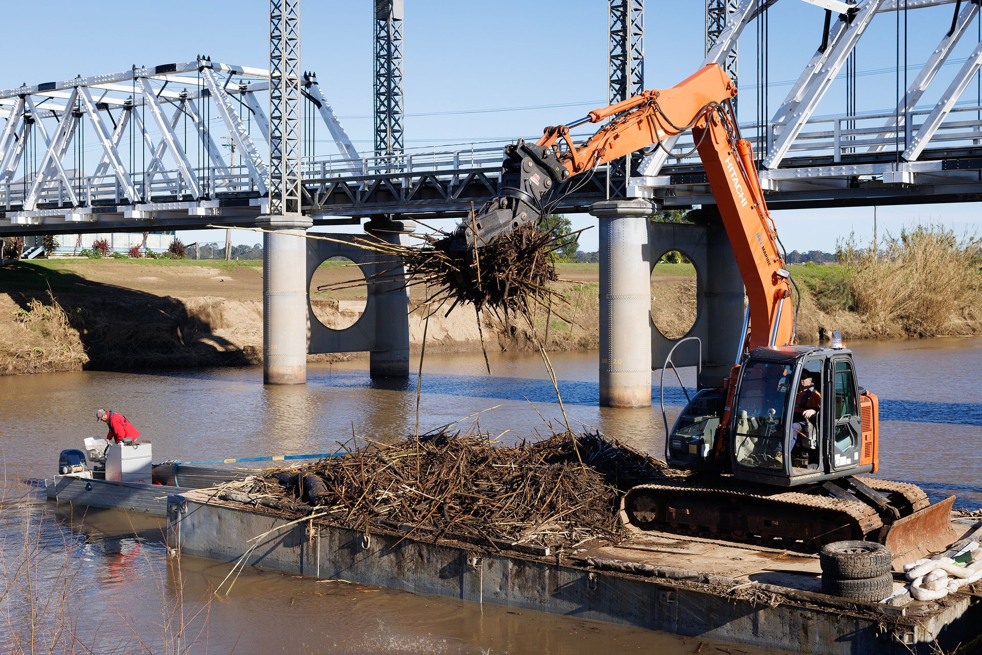 An Excavator on A Barge Clears Debris from A River Under a Metal Bridge — M&J Marine Services in Medowie, NSW