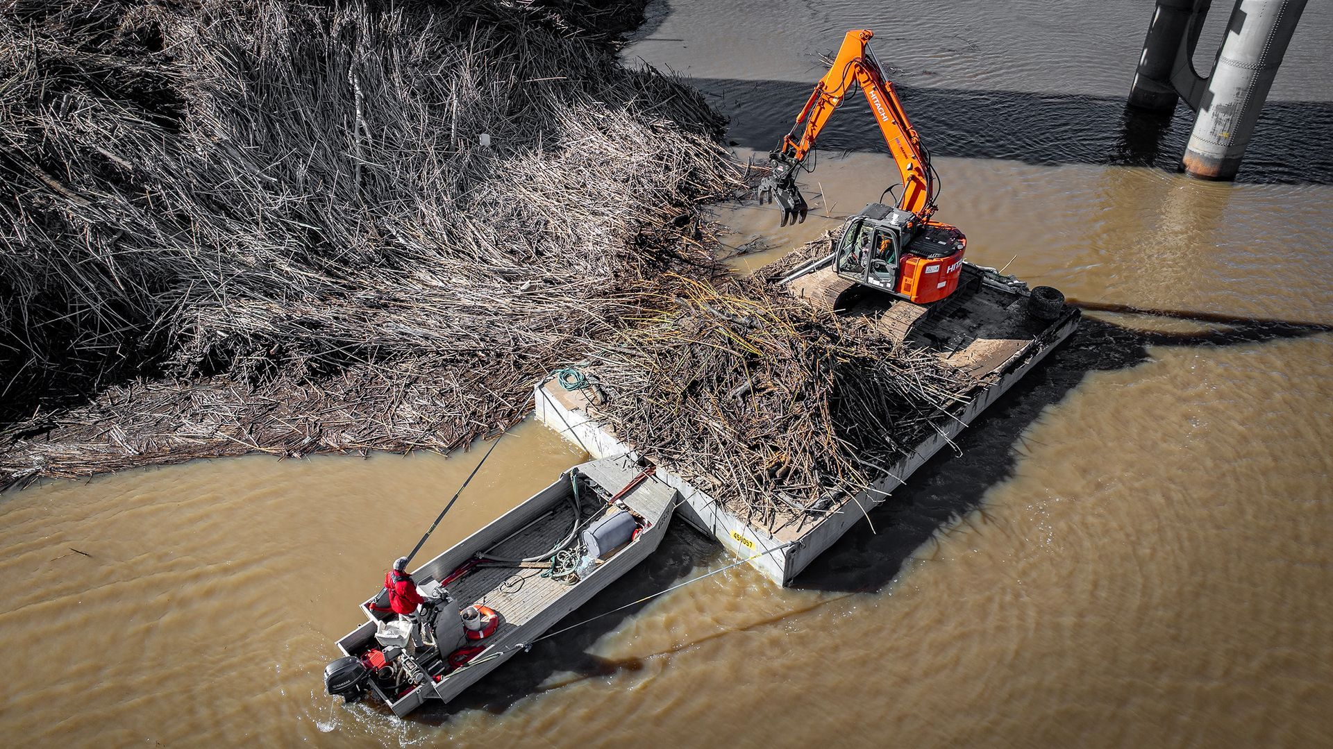 An Orange Excavator on A Barge Is Clearing Debris from A Muddy River — M&J Marine Services in Medowie, NSW