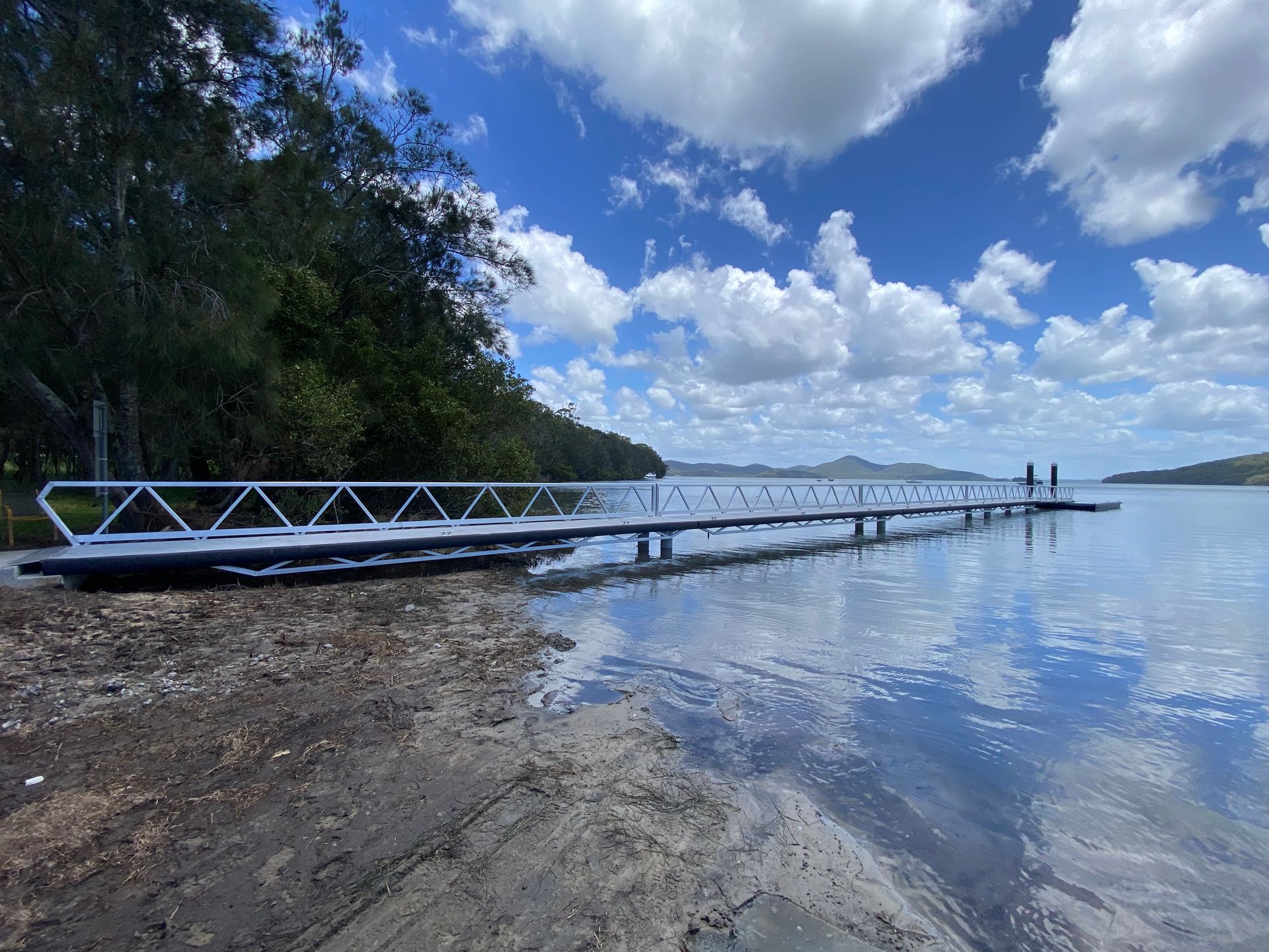 A Long Pier Extends Into a Calm Body of Water Under a Partly Cloudy Sky — M&J Marine Services in Newcastle, NSW