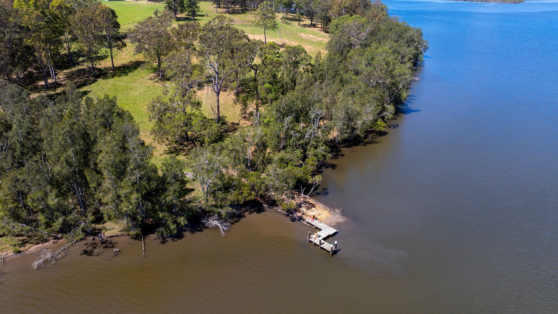 A Wooden Dock Extending from A Tree Lined Grassy Shore — M&J Marine Services in Medowie, NSW