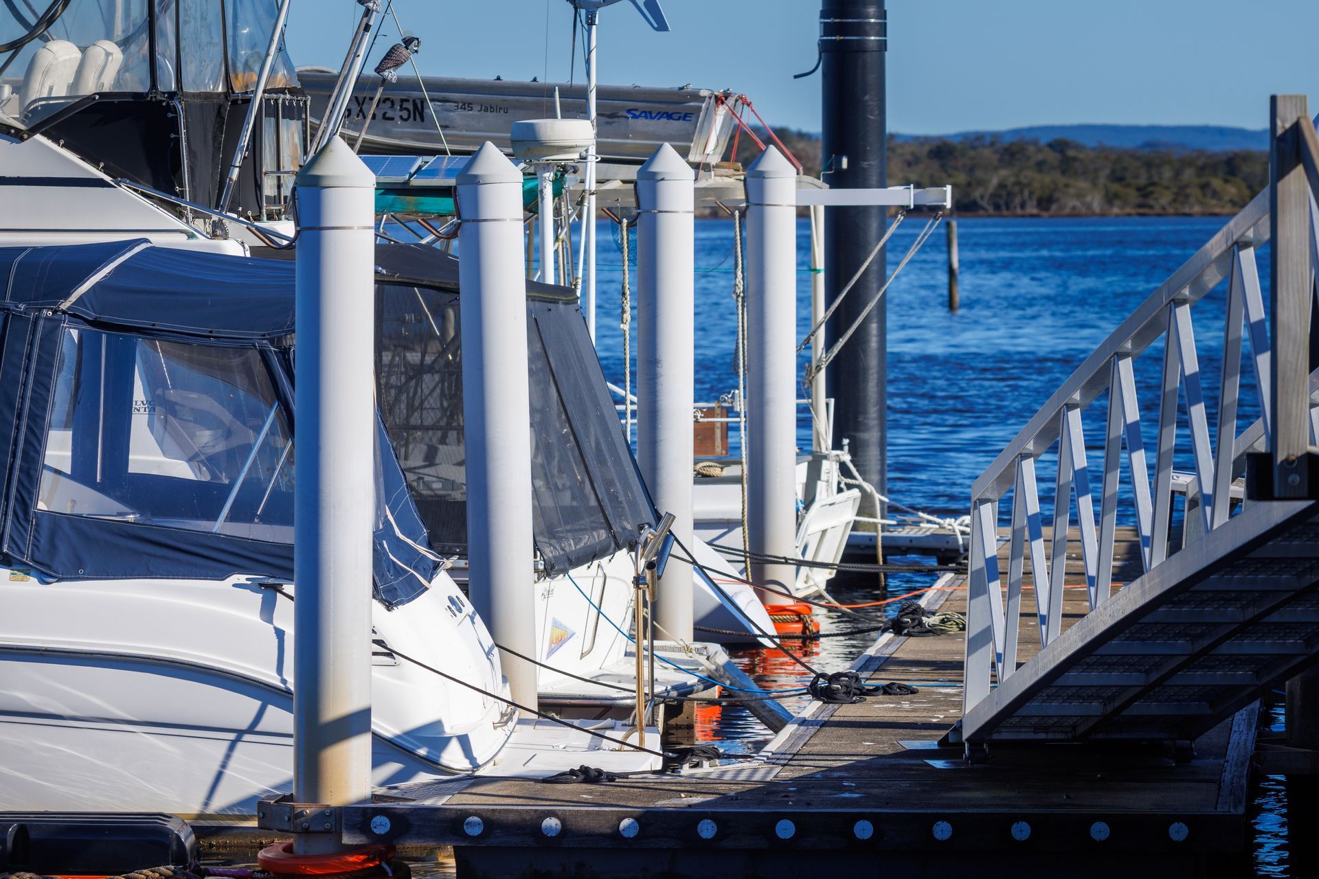 A White Boat Docked at A Marina Pier with White Support Pilings — M&J Marine Services in Lake Macquarie, NSW