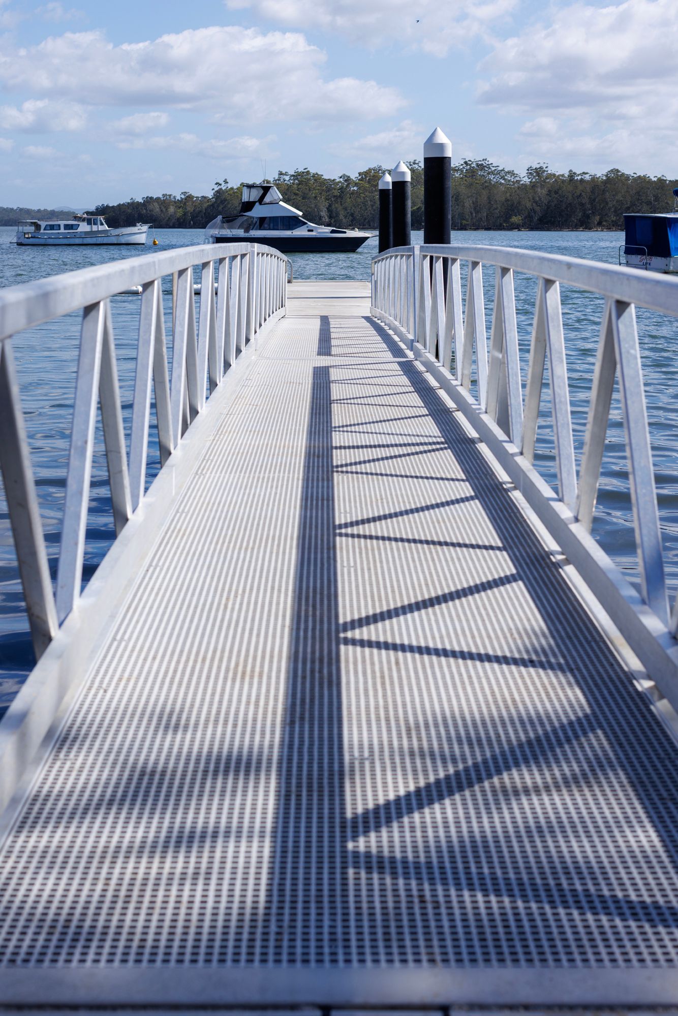 A Metal Walkway Extends Over Water Toward Wooden Pilings — M&J Marine Services in Newcastle, NSW