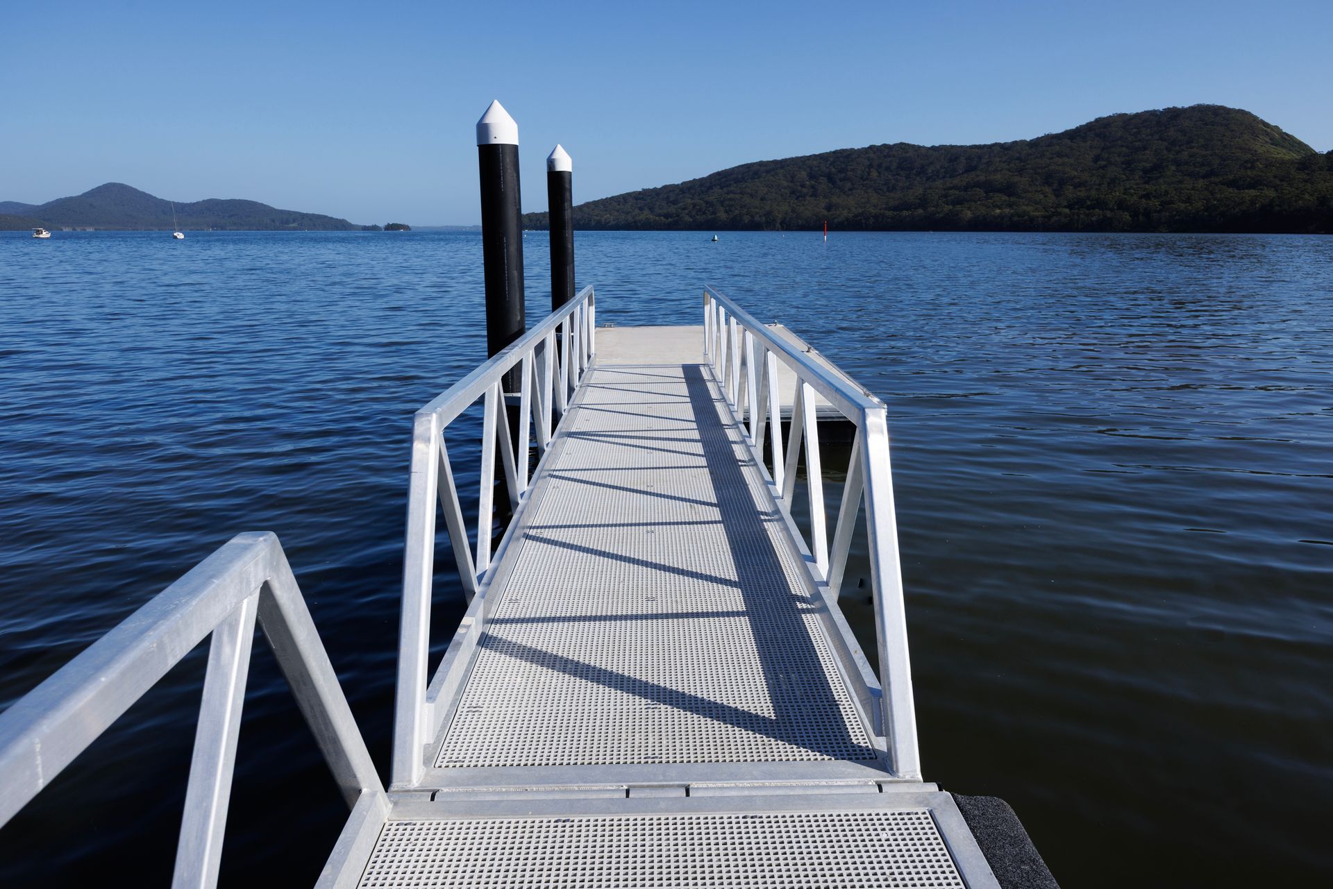 A Metal Walkway Extends Over Blue Water Toward Two Pilings — M&J Marine Services in Medowie, NSW