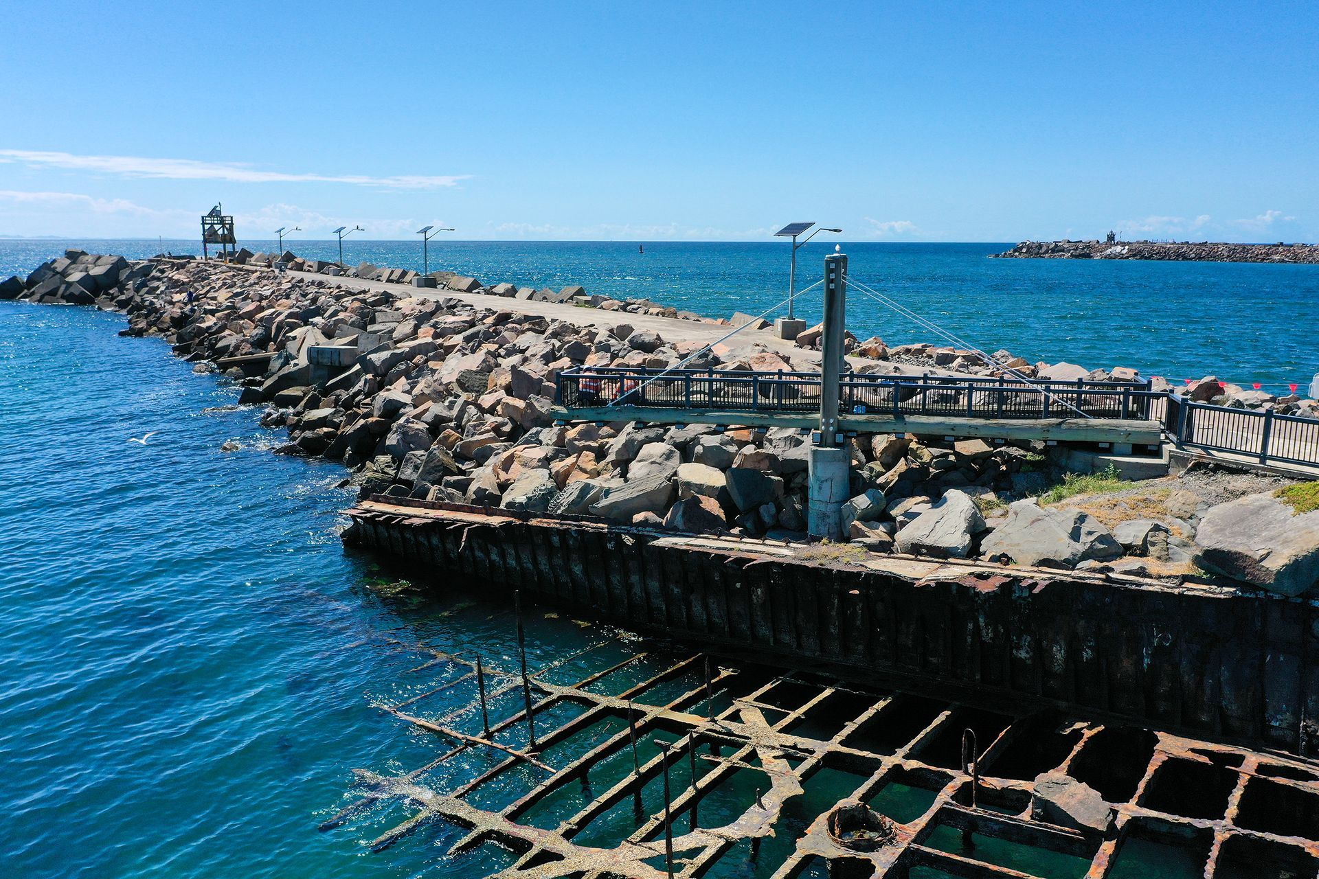 A Stone Breakwater Extends Into Deep Blue Ocean Water, with A Metal Grid Structure — M&J Marine Services in Coffs Harbour, NSW