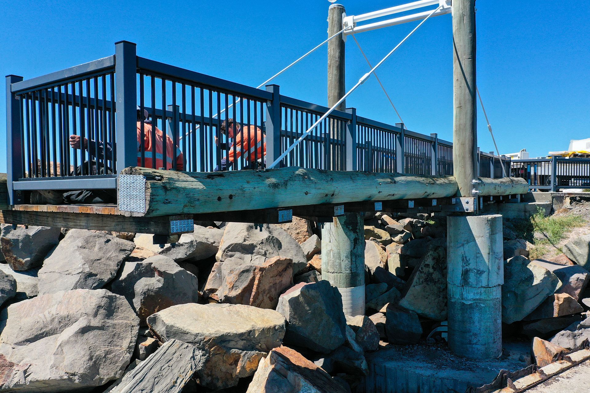 Two Workers on A Wooden Footbridge Over a Rocky Shoreline — M&J Marine Services in Medowie, NSW