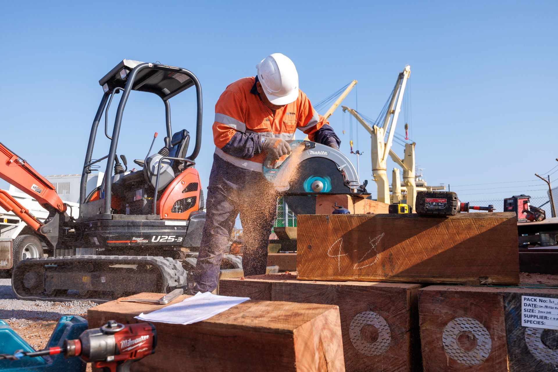 A Construction Worker in High-Visibility Gear Cuts a Large Wooden Beam — M&J Marine Services in Medowie, NSW