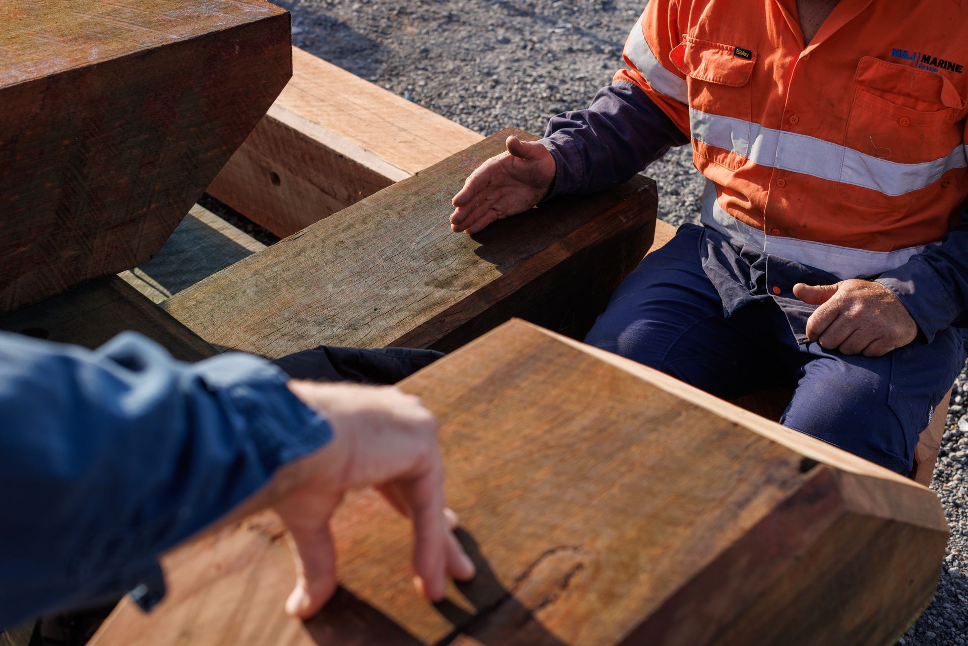 Two People Examine Large Wooden Beams in An Outdoor Workspace — M&J Marine Services in Newcastle, NSW