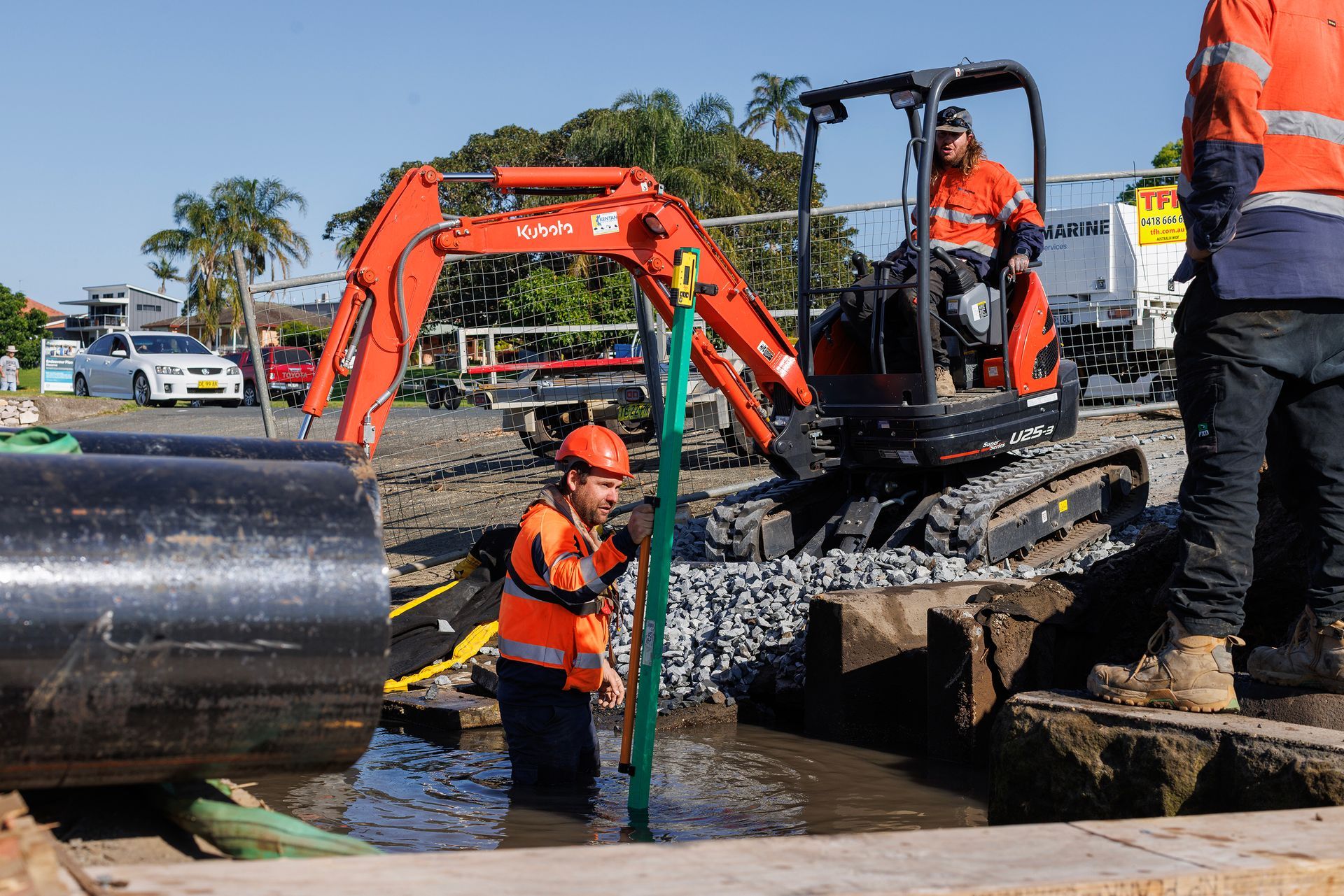 Workers in High Visibility Safety Gear Install a Large Pipe in A Muddy Trench — M&J Marine Services in Coffs Harbour, NSW