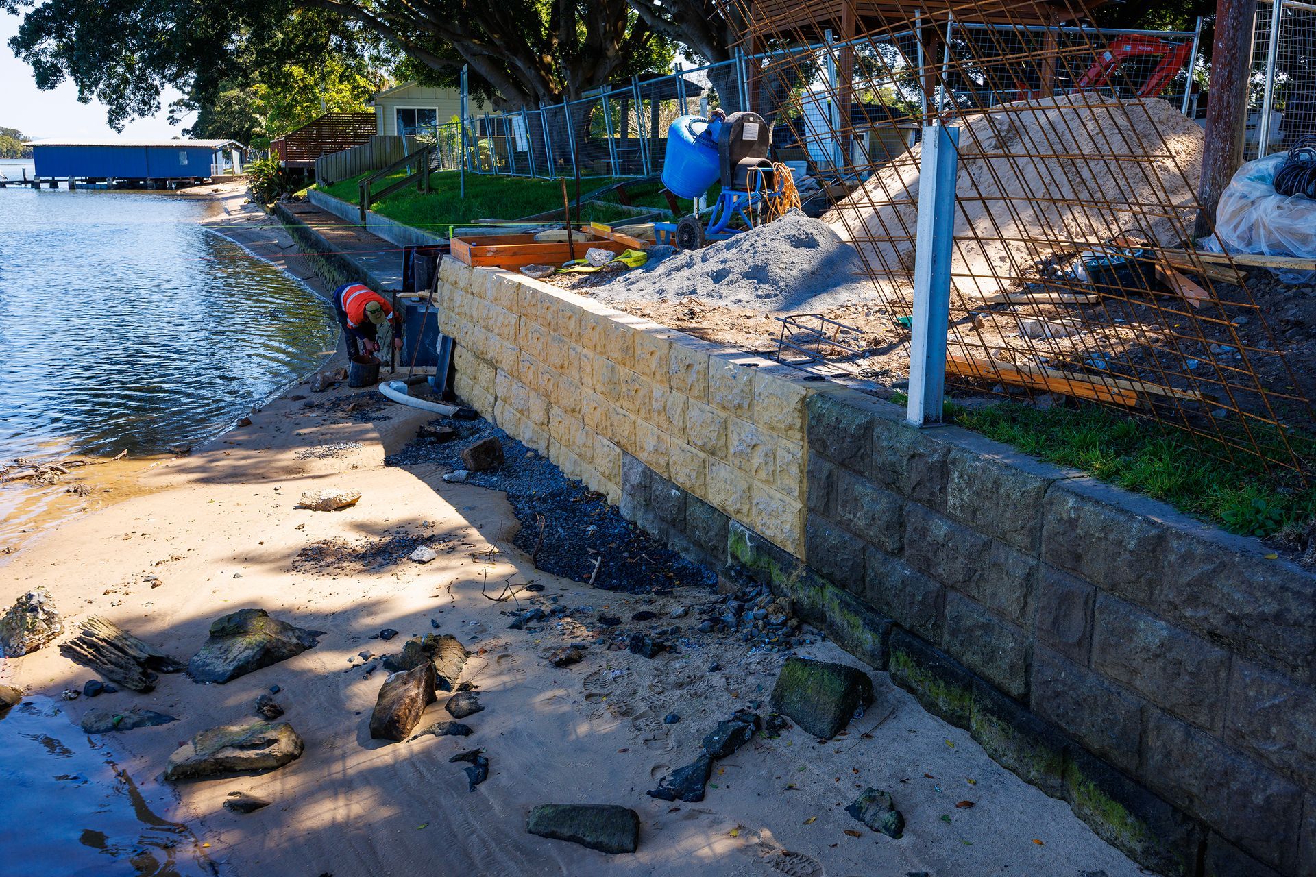 A Person Works on A Stone Retaining Wall Along a Sandy Shoreline — M&J Marine Services in Coffs Harbour, NSW