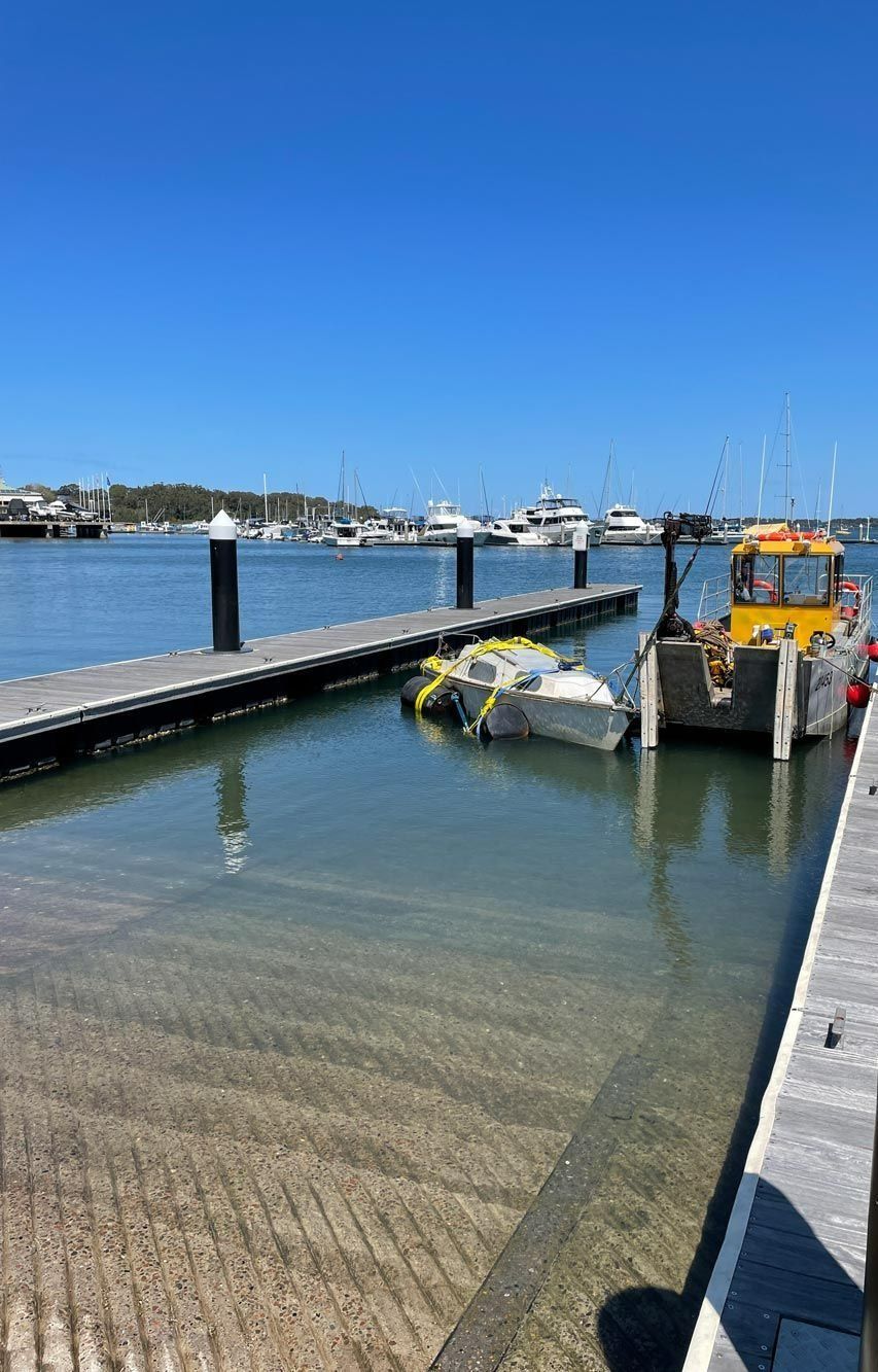 A Yellow Boat Next to A Pier with Another White Boat in The Water — M&J Marine Services in Newcastle, NSW