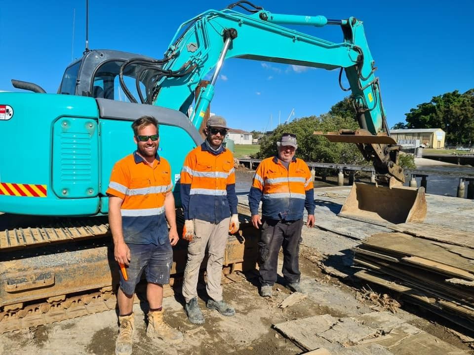Construction Workers Stand in Front of A Turquoise Excavator on A Construction Site — M&J Marine Services in Medowie, NSW
