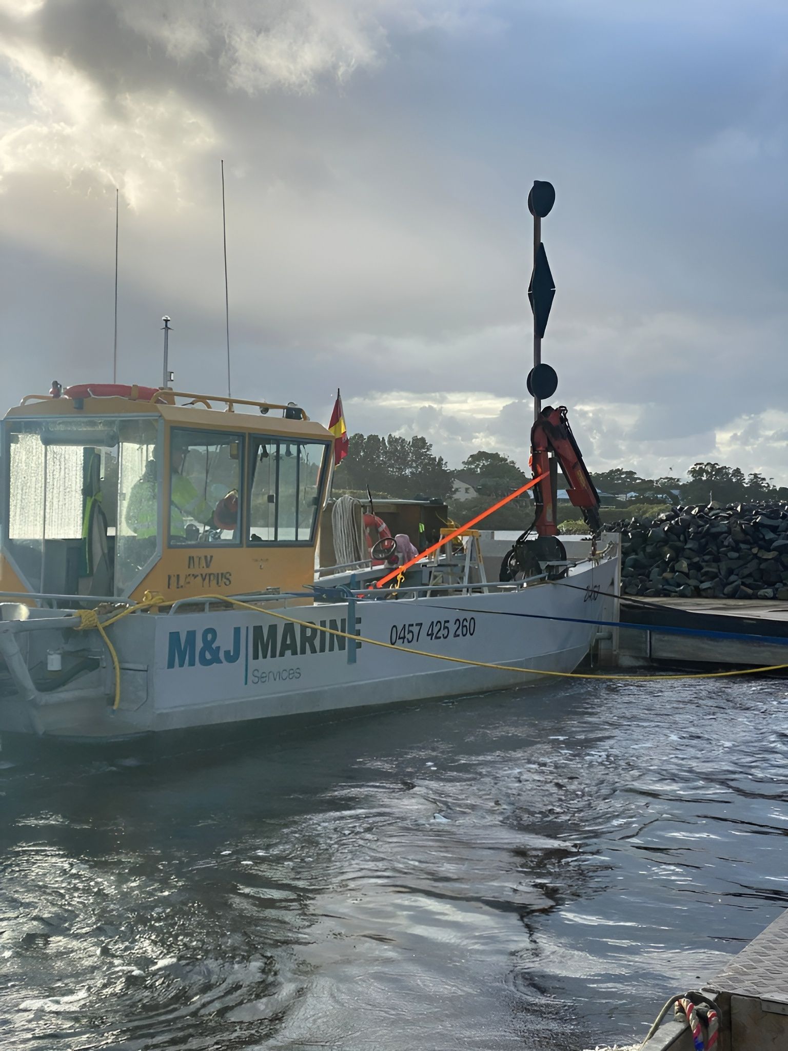 Boat with Crane, M&J Marine on Side, Beside a Dark, Rocky Pier — M&J Marine Services in Medowie, NSW