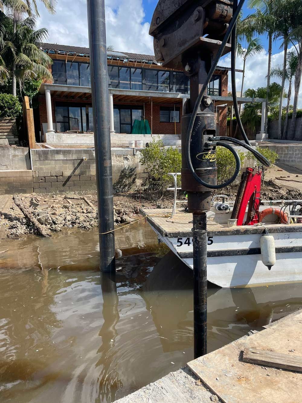 Construction Machinery Drilling Near Water with A House in The Background — M&J Marine Services in Medowie, NSW