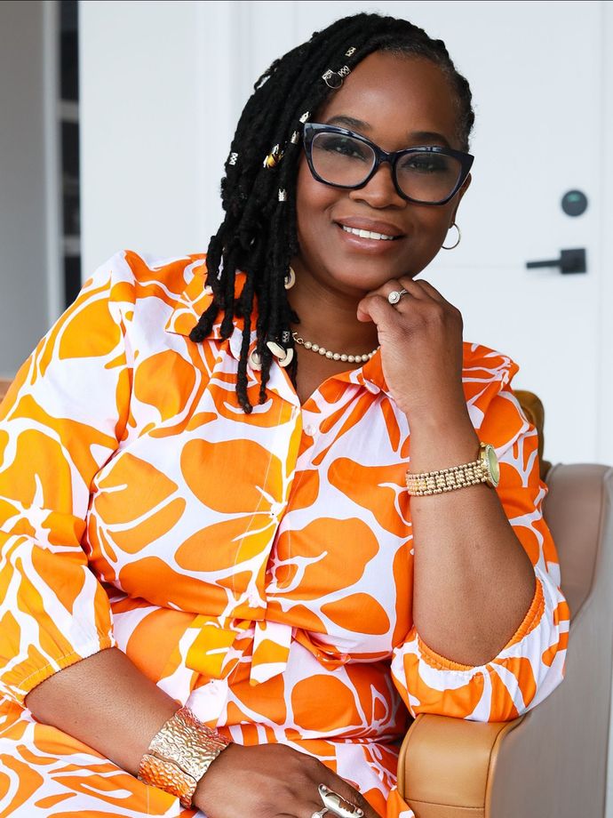 A woman wearing glasses and an orange and white dress is sitting in a chair.