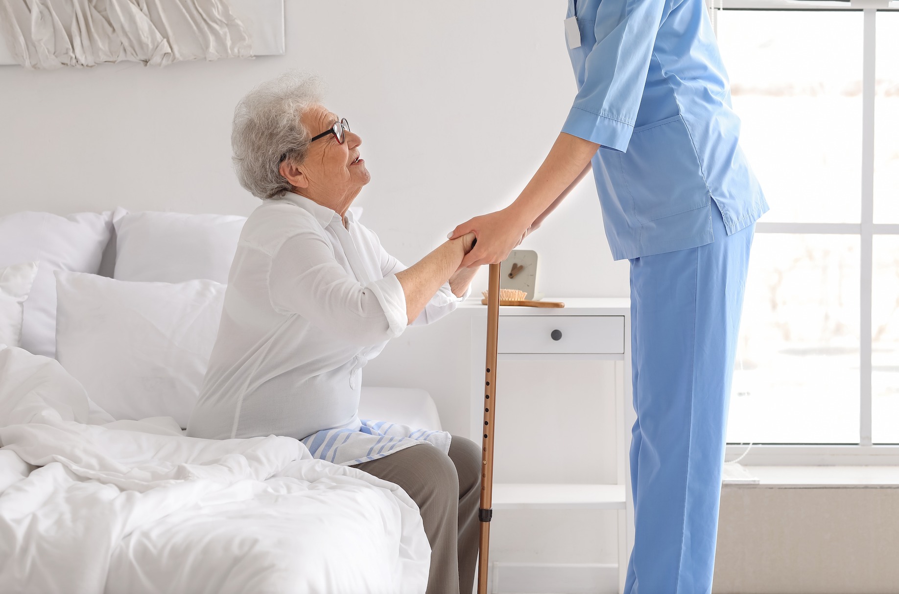 An elderly woman is sitting on a bed holding the hand of a nurse.