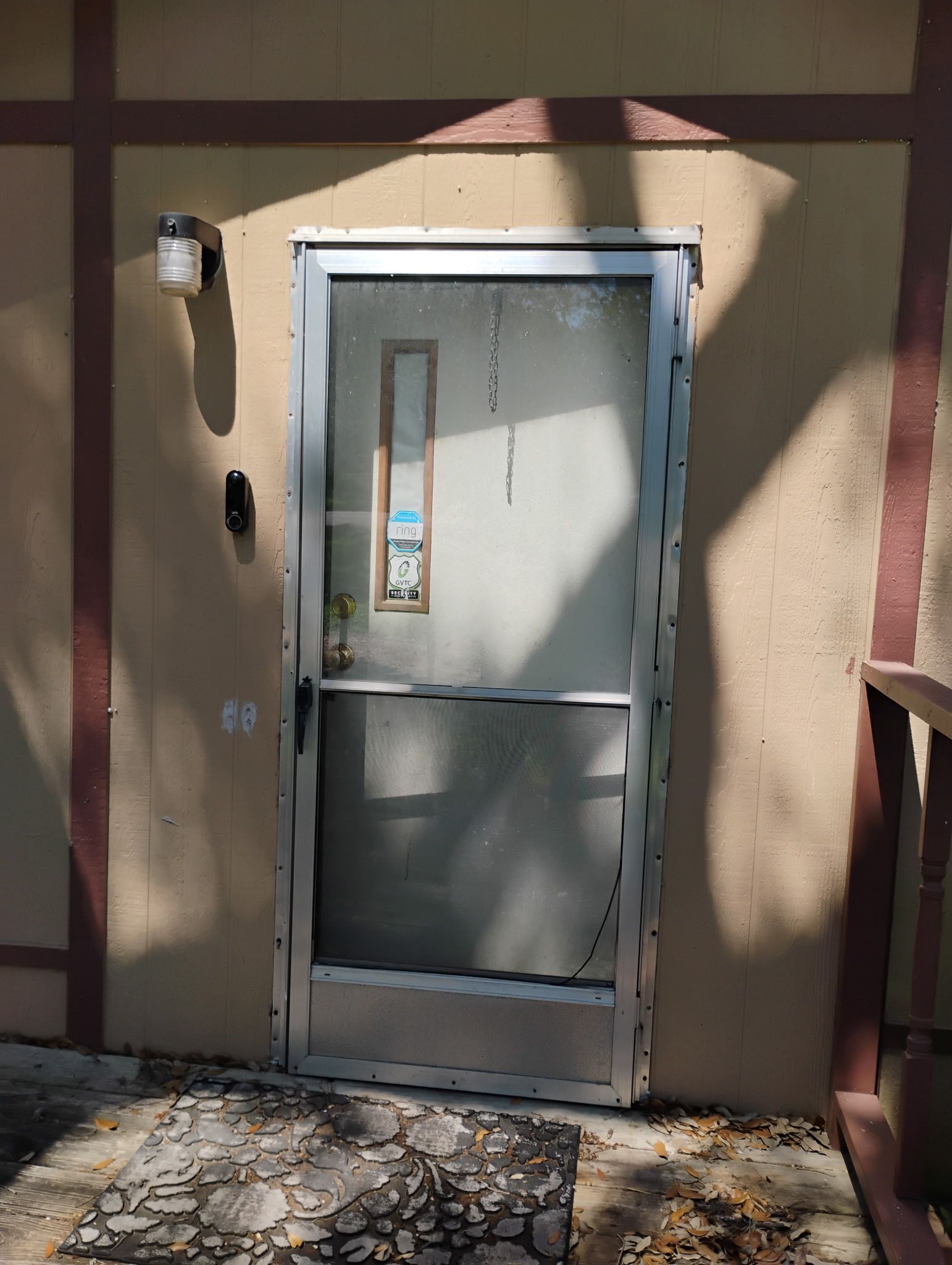 Beige exterior wall with a glass door, wall light, and cracked stone patio in sunlight.