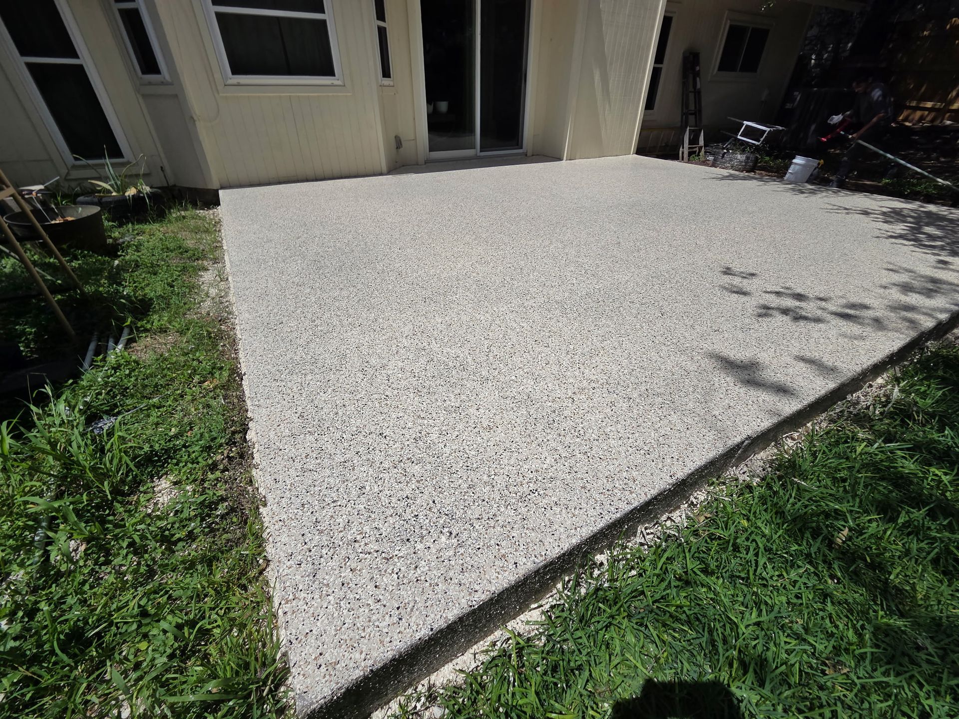 Gravel patio beside a beige building, bordered by green grass in bright sunlight
