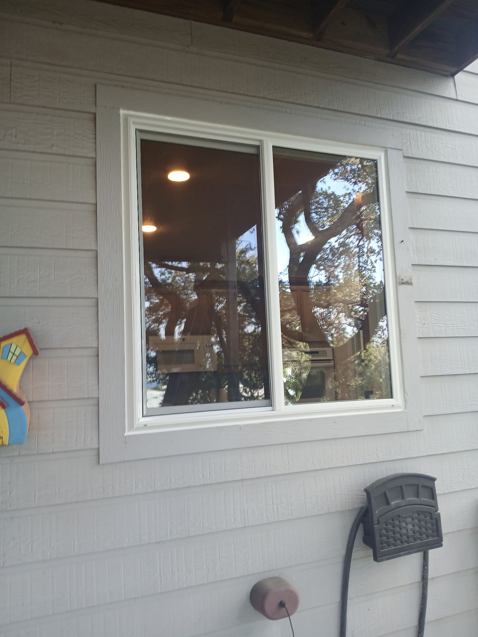 White-framed window on a gray house exterior with reflections and a wall-mounted basket nearby.