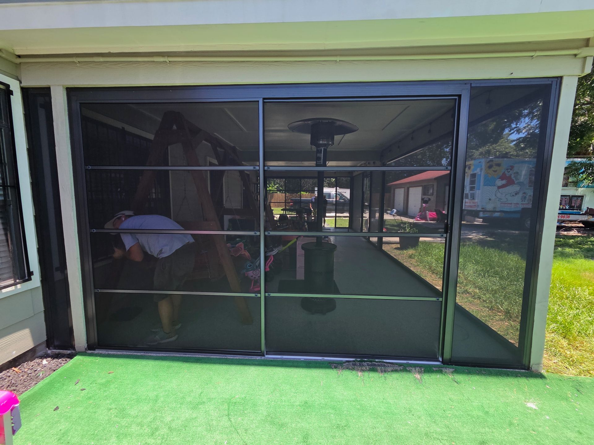 Black mesh patio screen enclosure with reflected yard and green turf in front