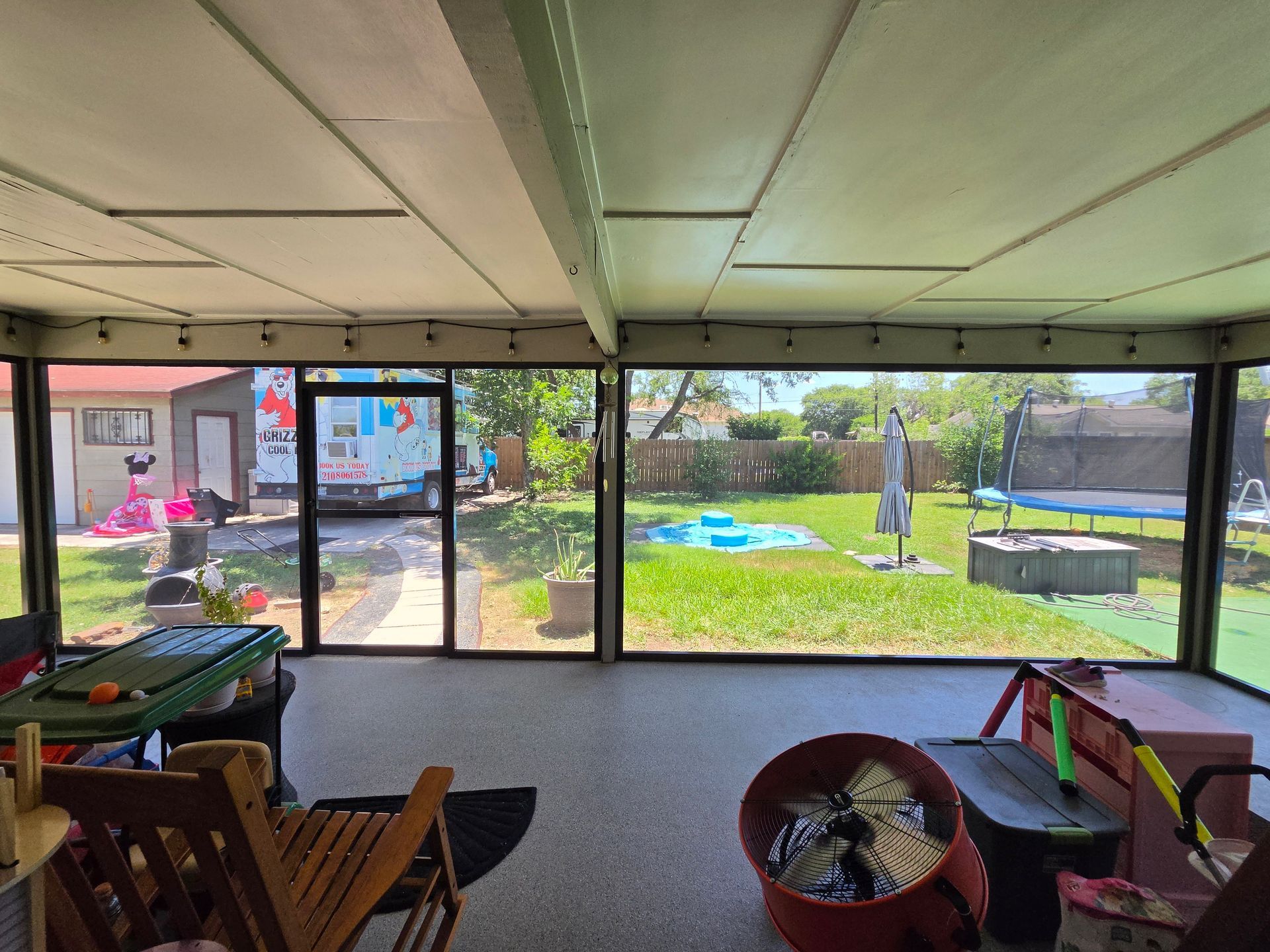 Indoor patio with floor-to-ceiling windows overlooking a sunny backyard with grass and trees.