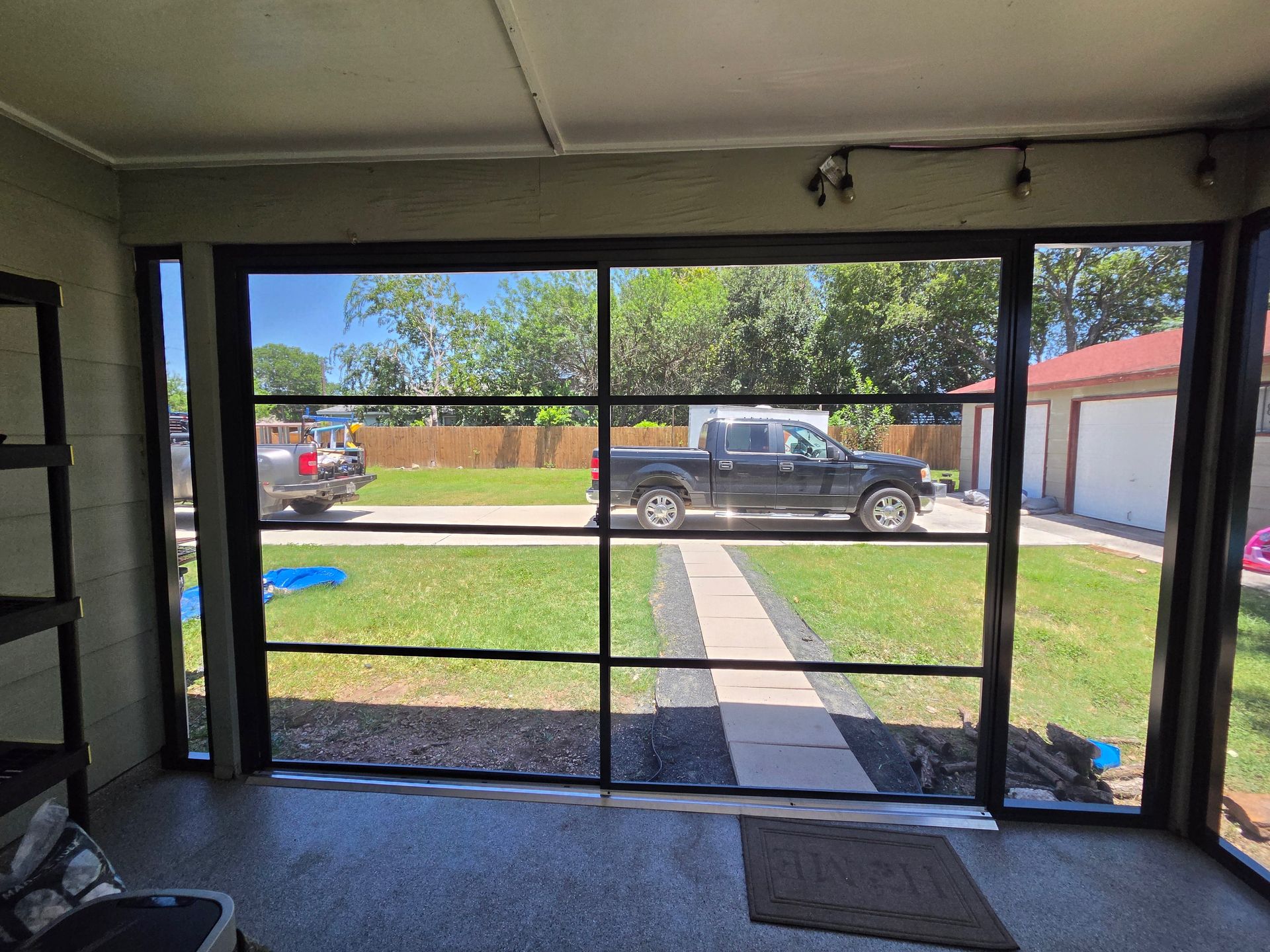 View from a garage opening to a suburban yard, sidewalk, and parked pickup truck across the street