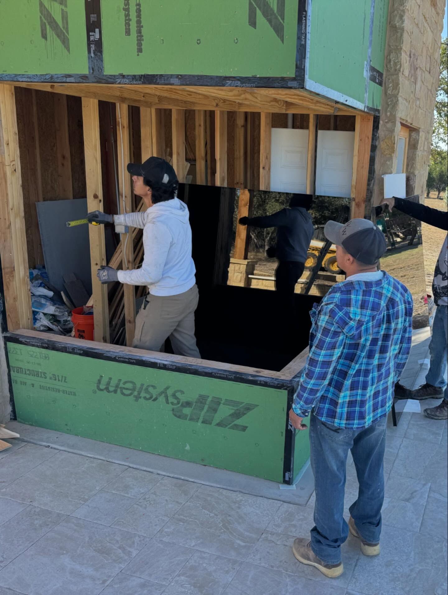 Two people installing insulation on a house wall framed in wood and green sheathing.