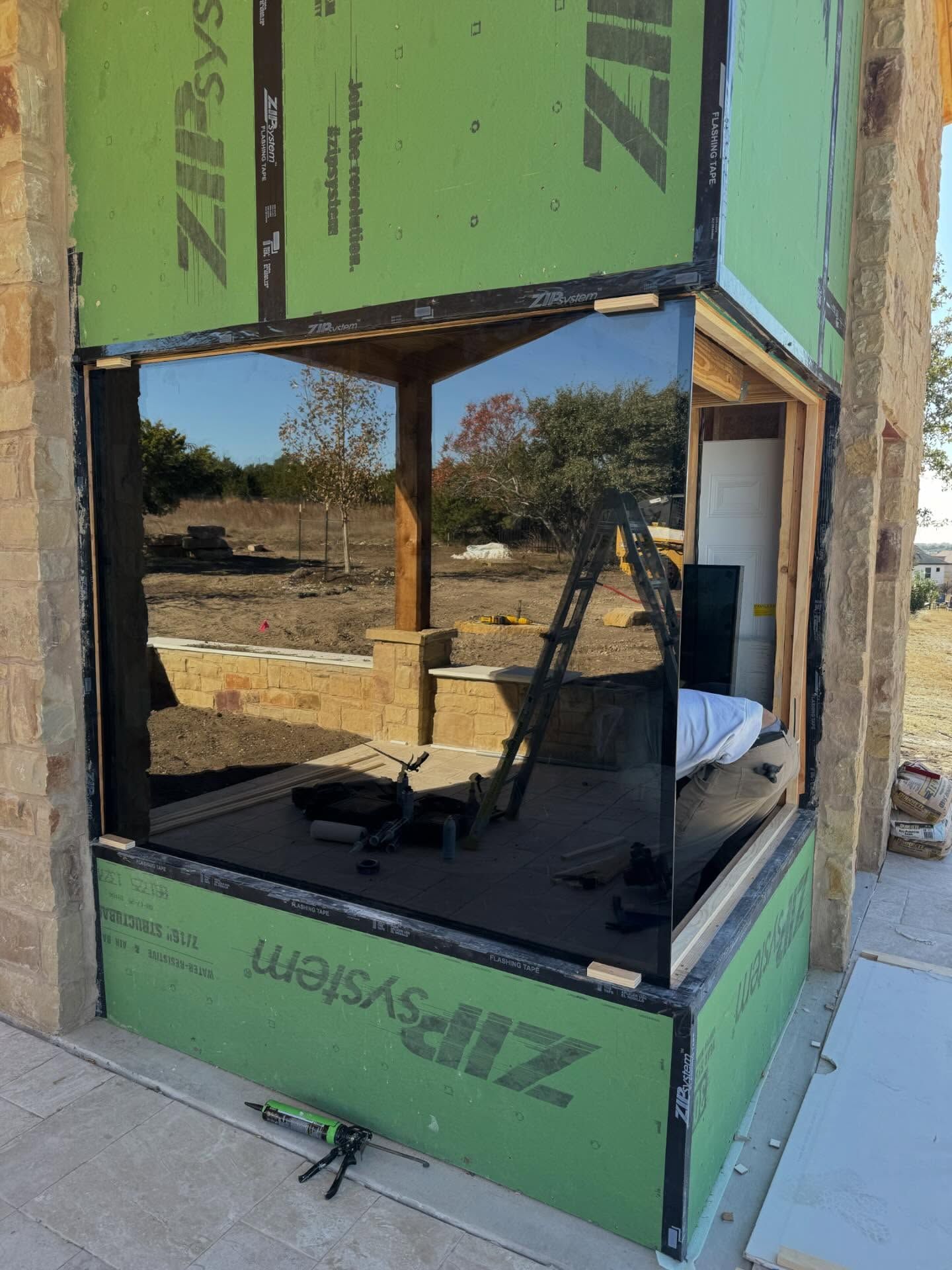 Green-framed glass corner booth under construction at an outdoor site, with tools inside and reflective windows.