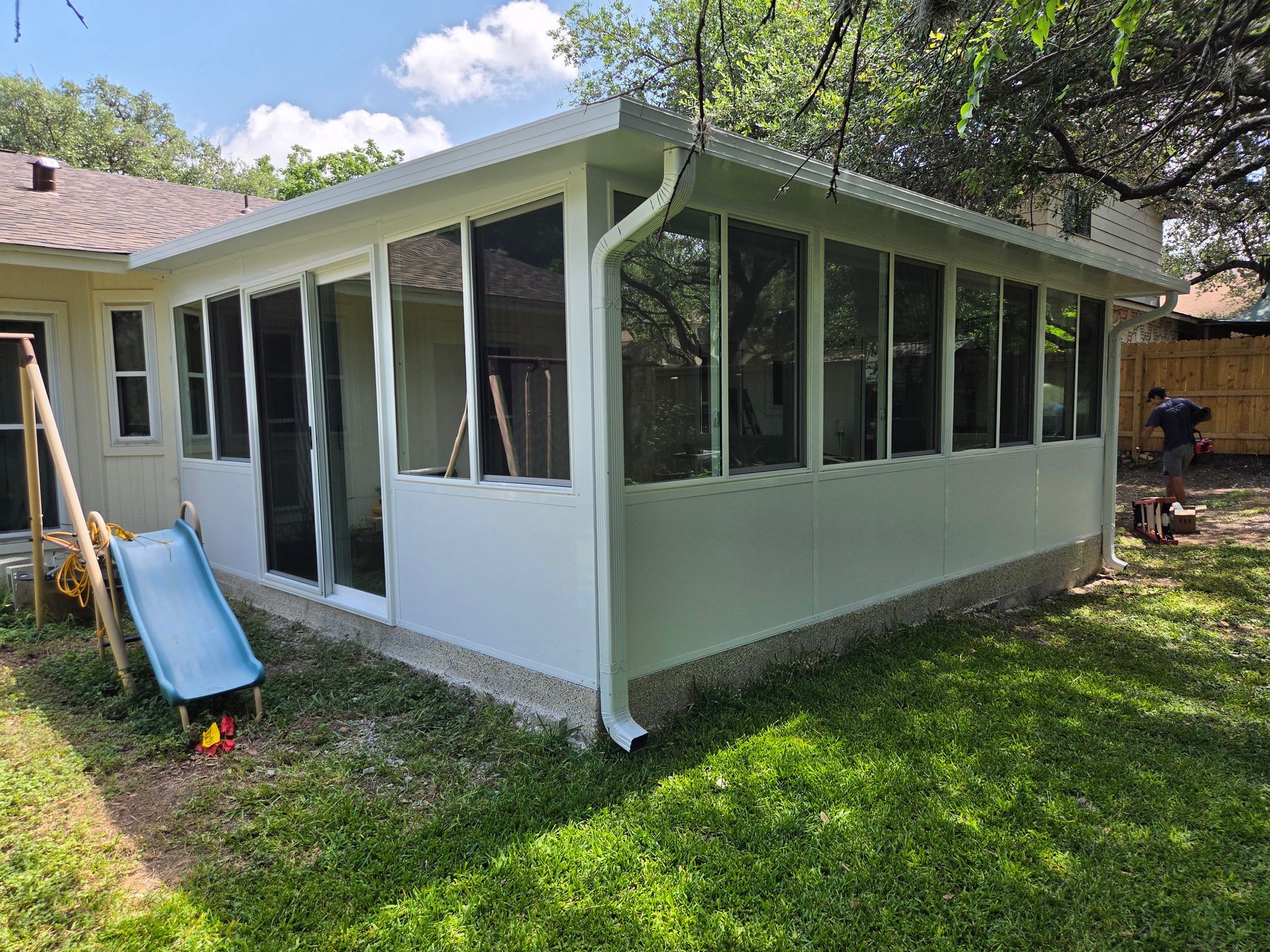 White screened porch addition on a house, with many windows, a blue slide, and a grassy backyard.