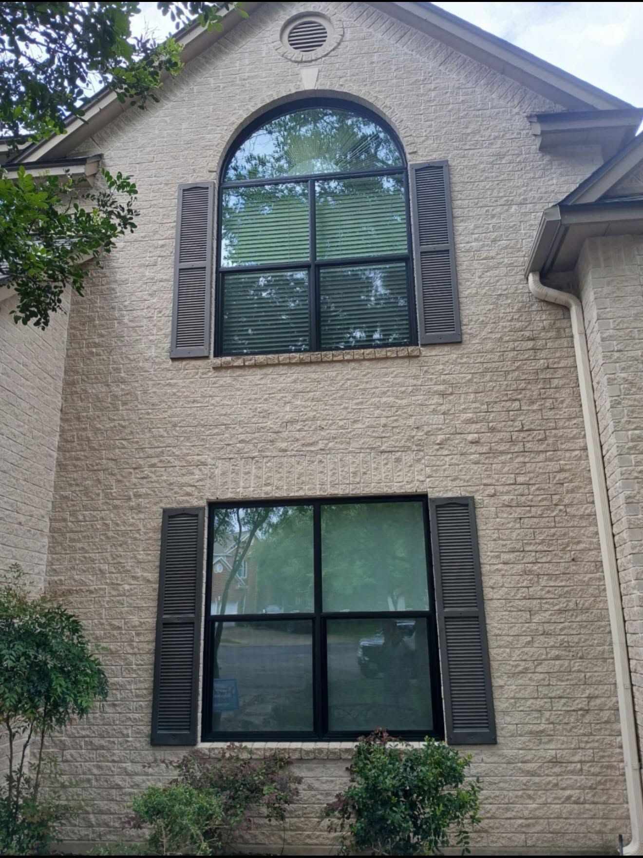 Two-story beige house exterior with arched upper window and dark shutters under a gabled roof.