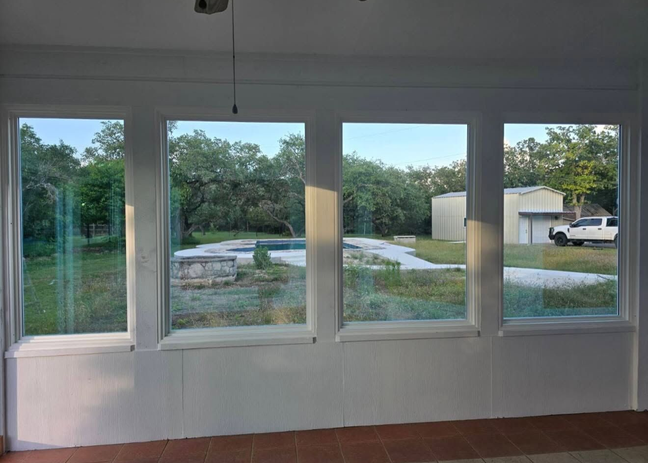 Large windows overlooking a grassy yard, trees, and a parked white truck outside.