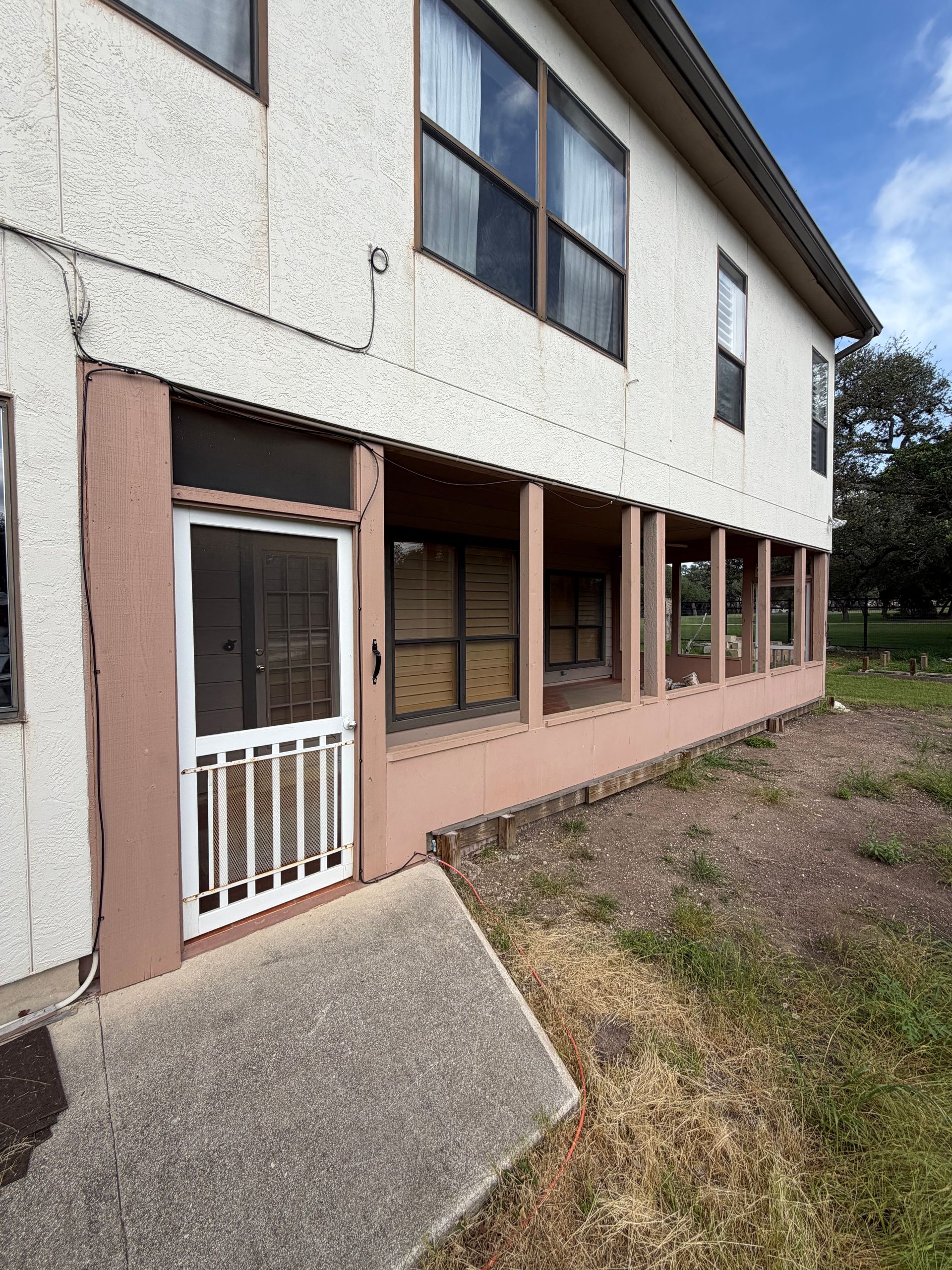 Exterior of a two-story building with a white and pink facade, screened porch, and concrete steps.