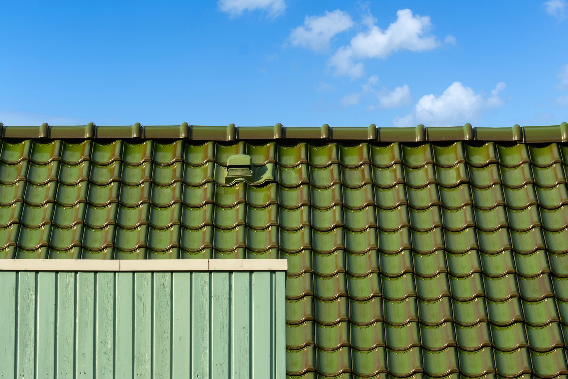Green tiled roof under a blue sky with scattered clouds, with a light green wall in the foreground