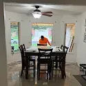 Dining room with dark table and chairs facing a bright window, person in orange shirt seated at the table