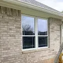 Brick house exterior with two white-framed windows and a beige gutter under the roofline