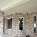 Brick house porch with beige ceiling and three windows on the exterior wall