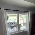 White-trimmed window with sheer curtains looking out onto a patio and garden.